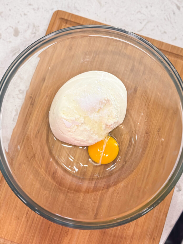 Ricotta cheese and egg in a glass mixing bowl before getting whisked.