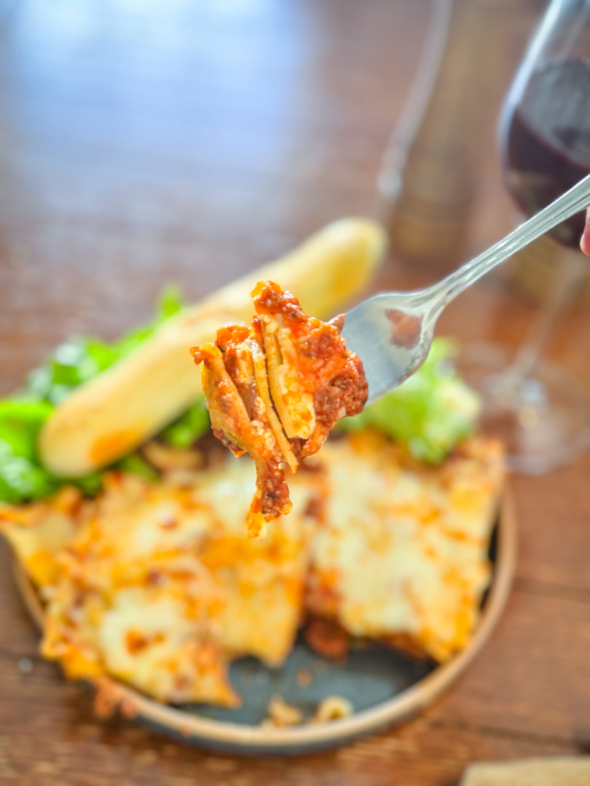 A forkful of oven baked lasagna hovering over a plate.