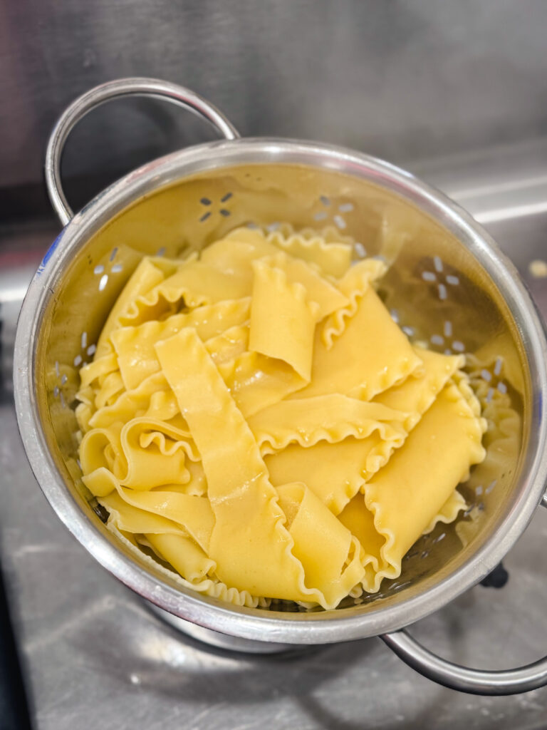 Cooked lasagna noodles in a colander in the sink.