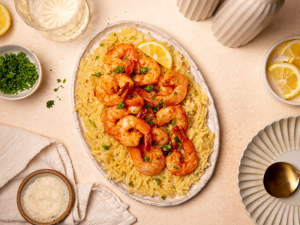 Roasted shrimp and orzo on a serving plate with lemon wedges and garnish.