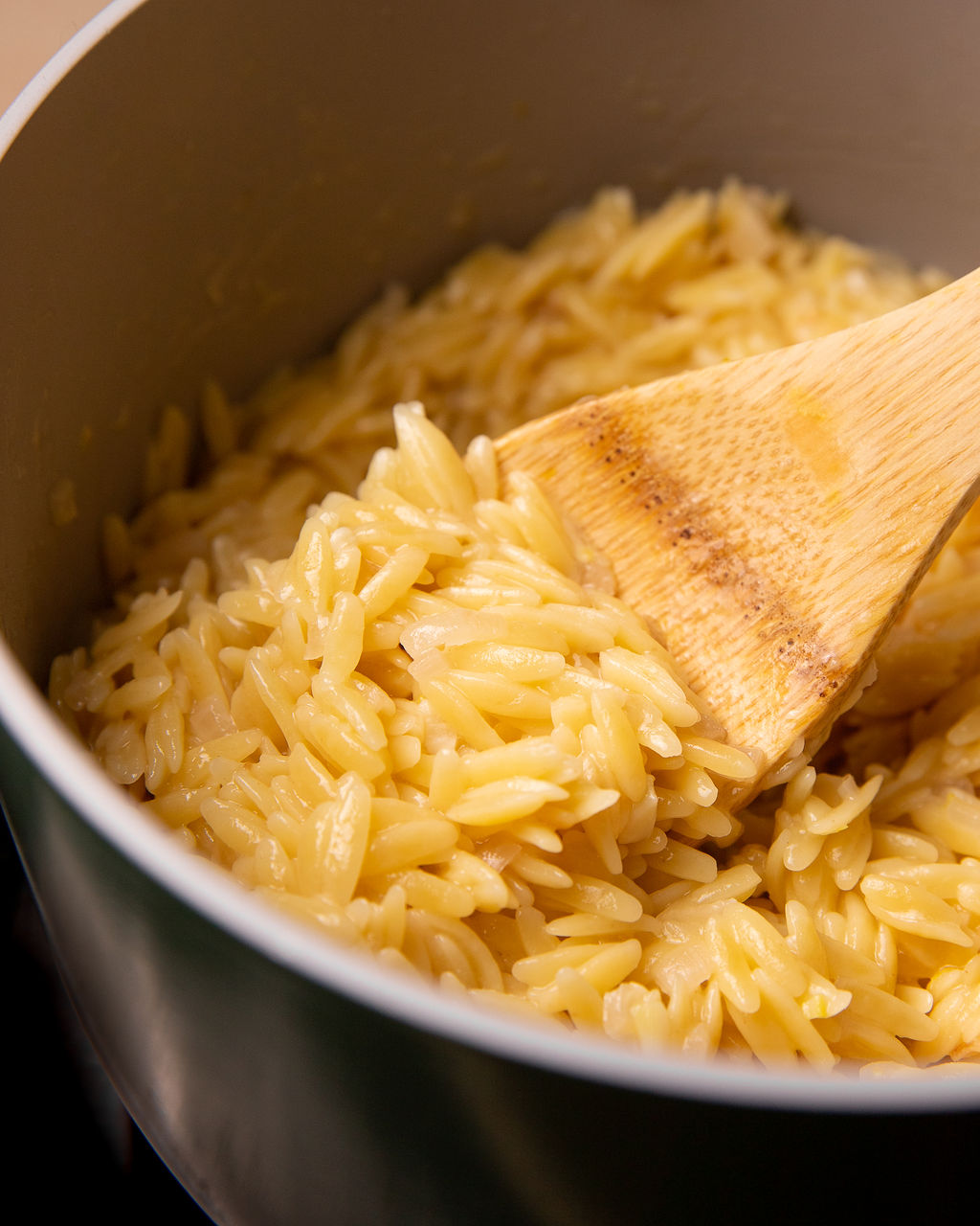 A wooden spoonful of orzo in a pot.