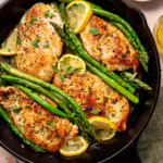 Lemon herb chicken with asparagus on a skillet ready to eat with lemon wedges as garnish.