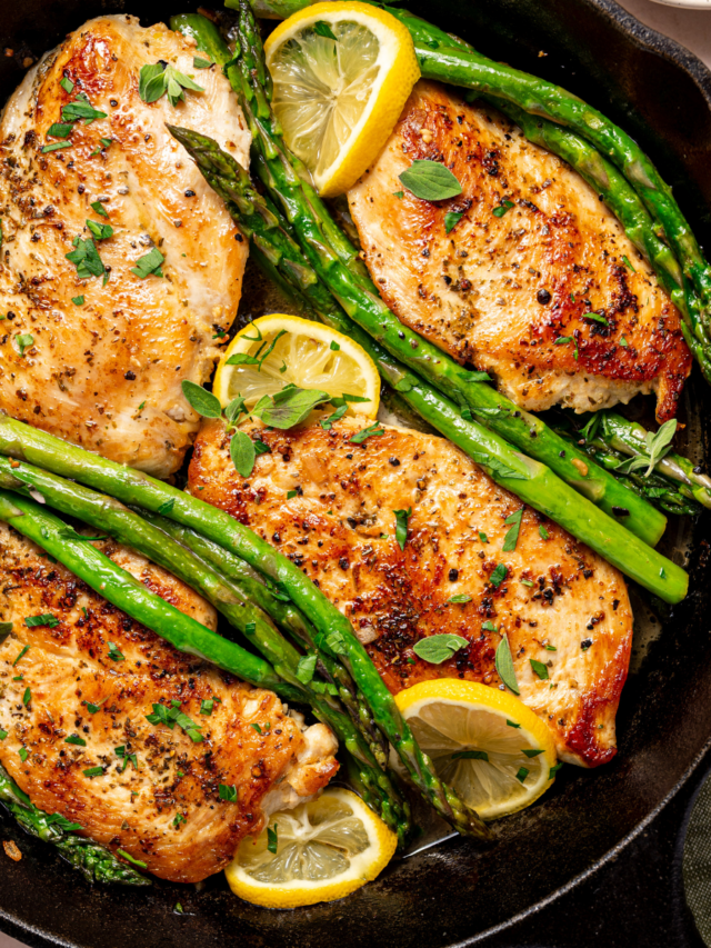 Lemon herb chicken with asparagus on a skillet ready to eat with lemon wedges as garnish.