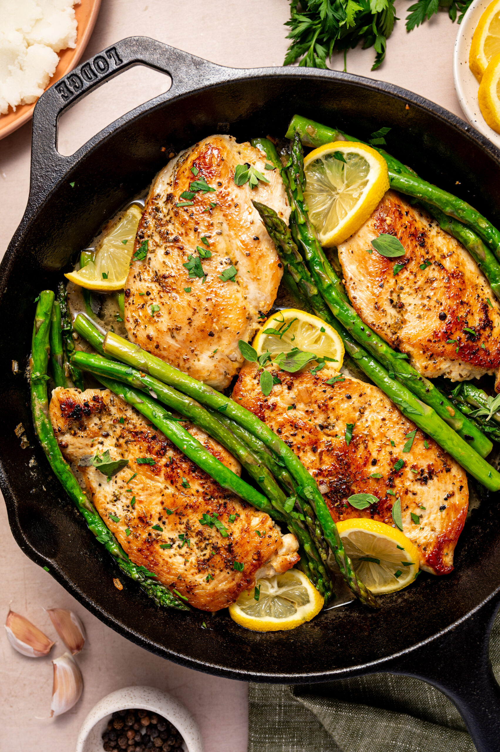 Lemon herb chicken with asparagus on a skillet ready to eat with lemon wedges as garnish.