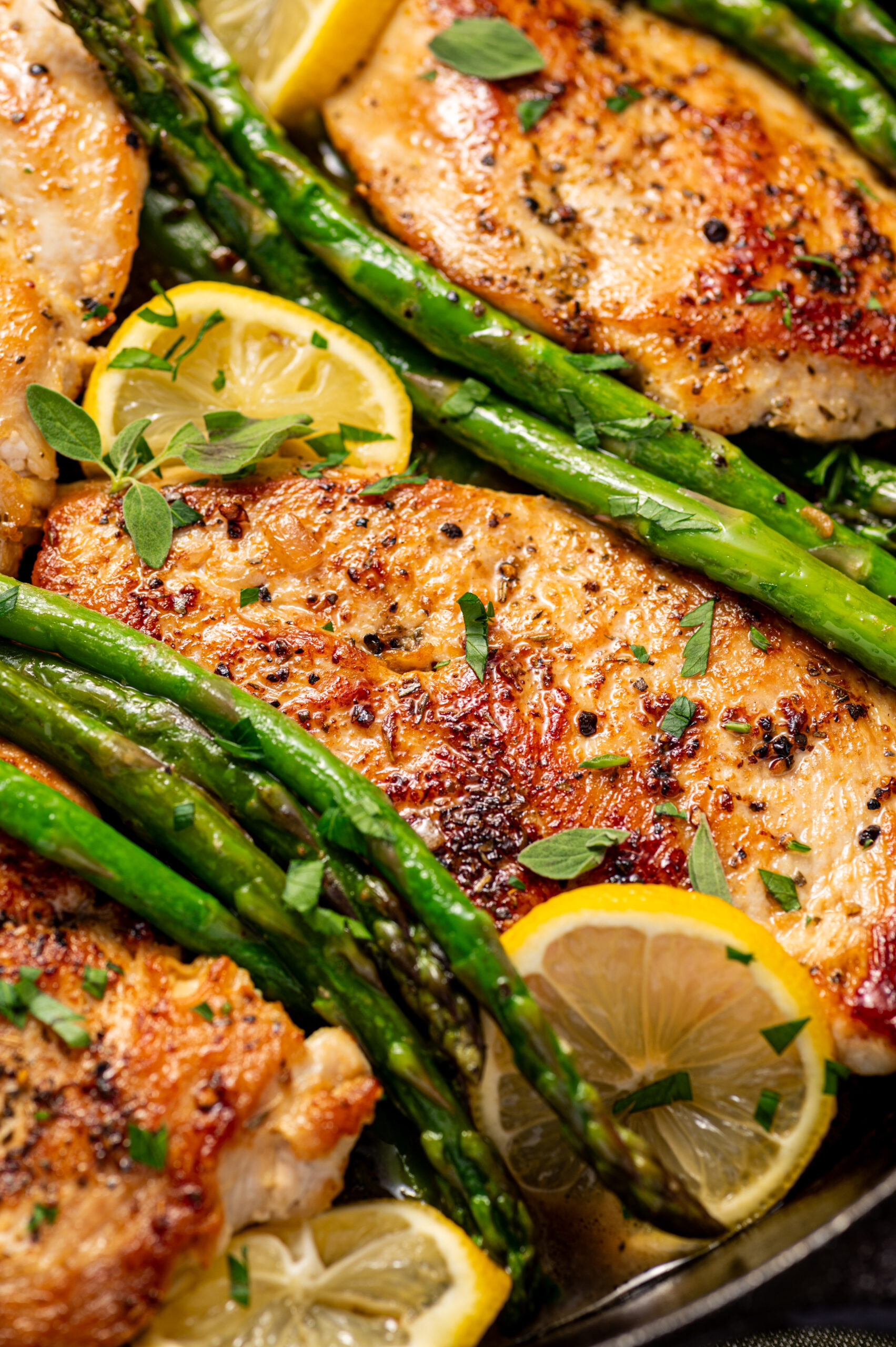 Lemon herb chicken with asparagus on a skillet with lemon wedges.