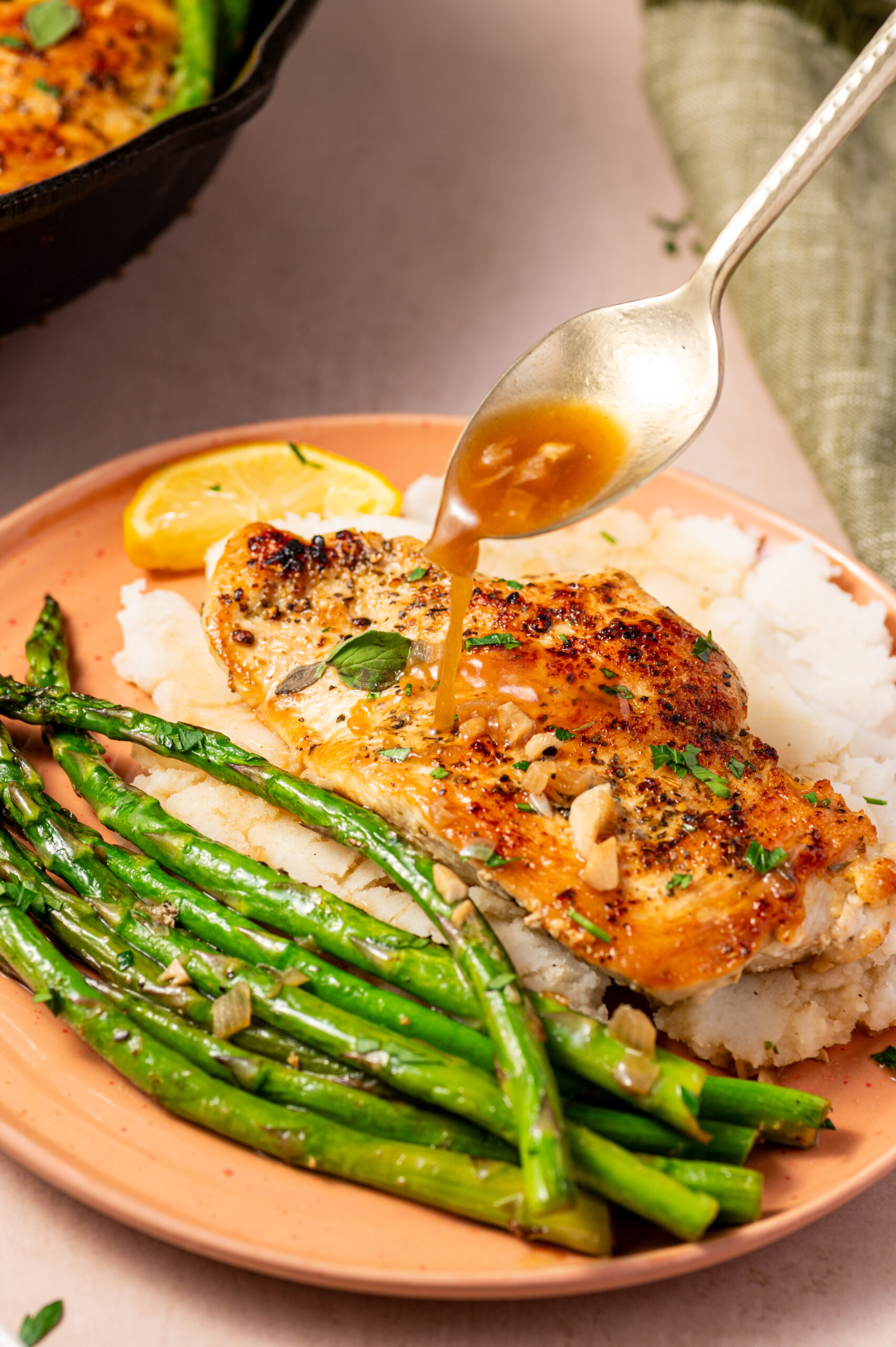 Spooning delicious lemon sauce on a plate of lemon herb chicken with asparagus.
