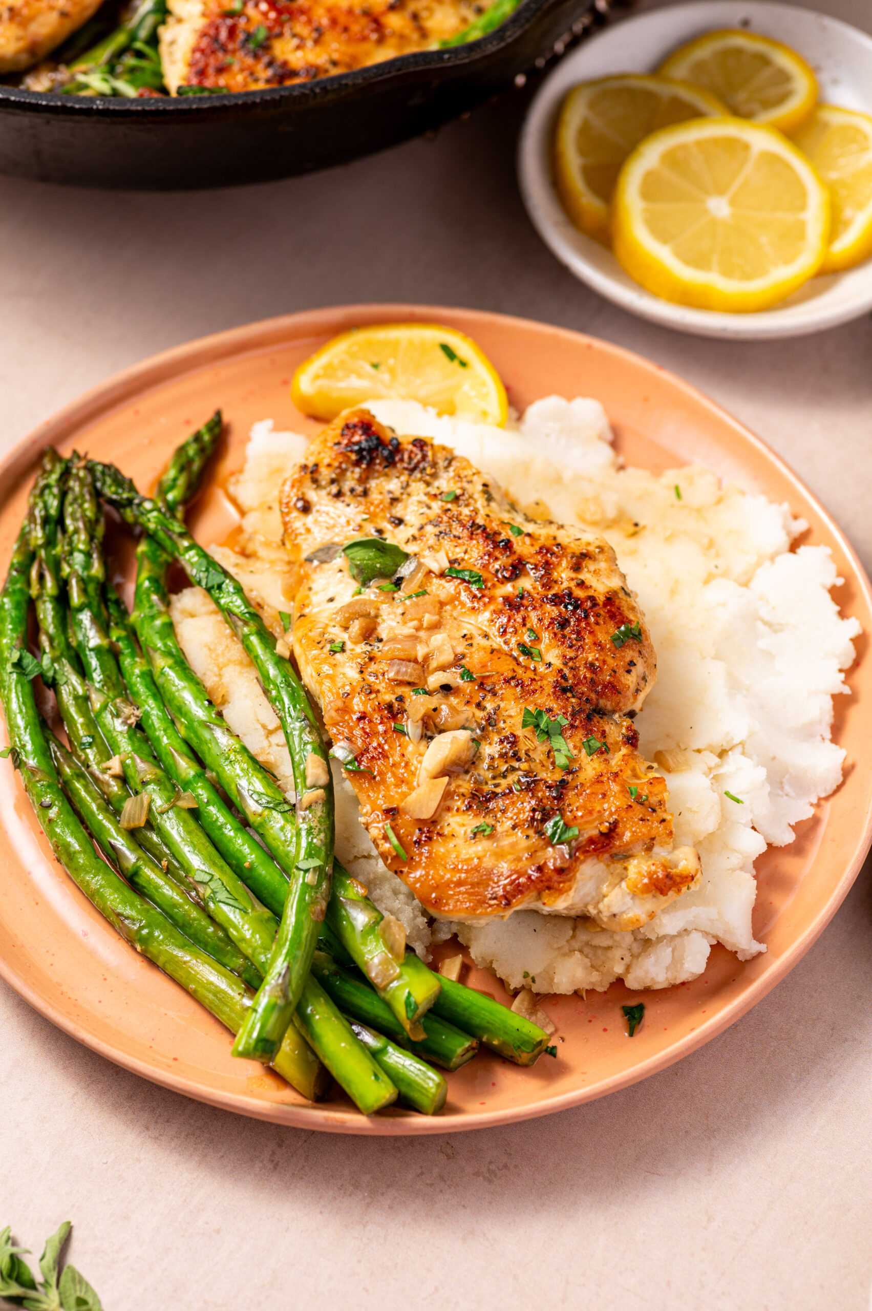 A serving of lemon herb chicken with asparagus on a plate with a side of potatoes.
