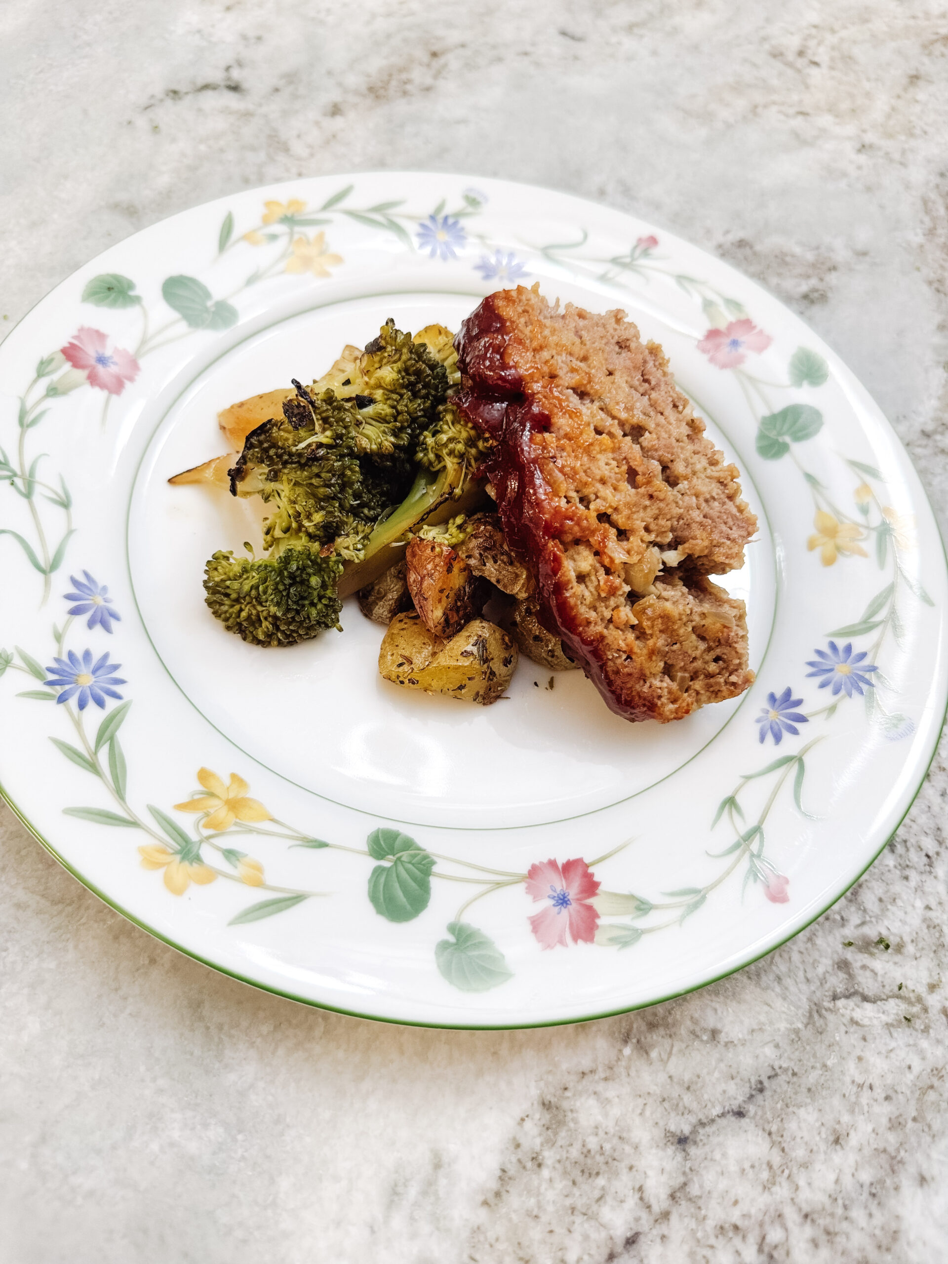 A serving of classic meatloaf on a plate with a side of veggies.