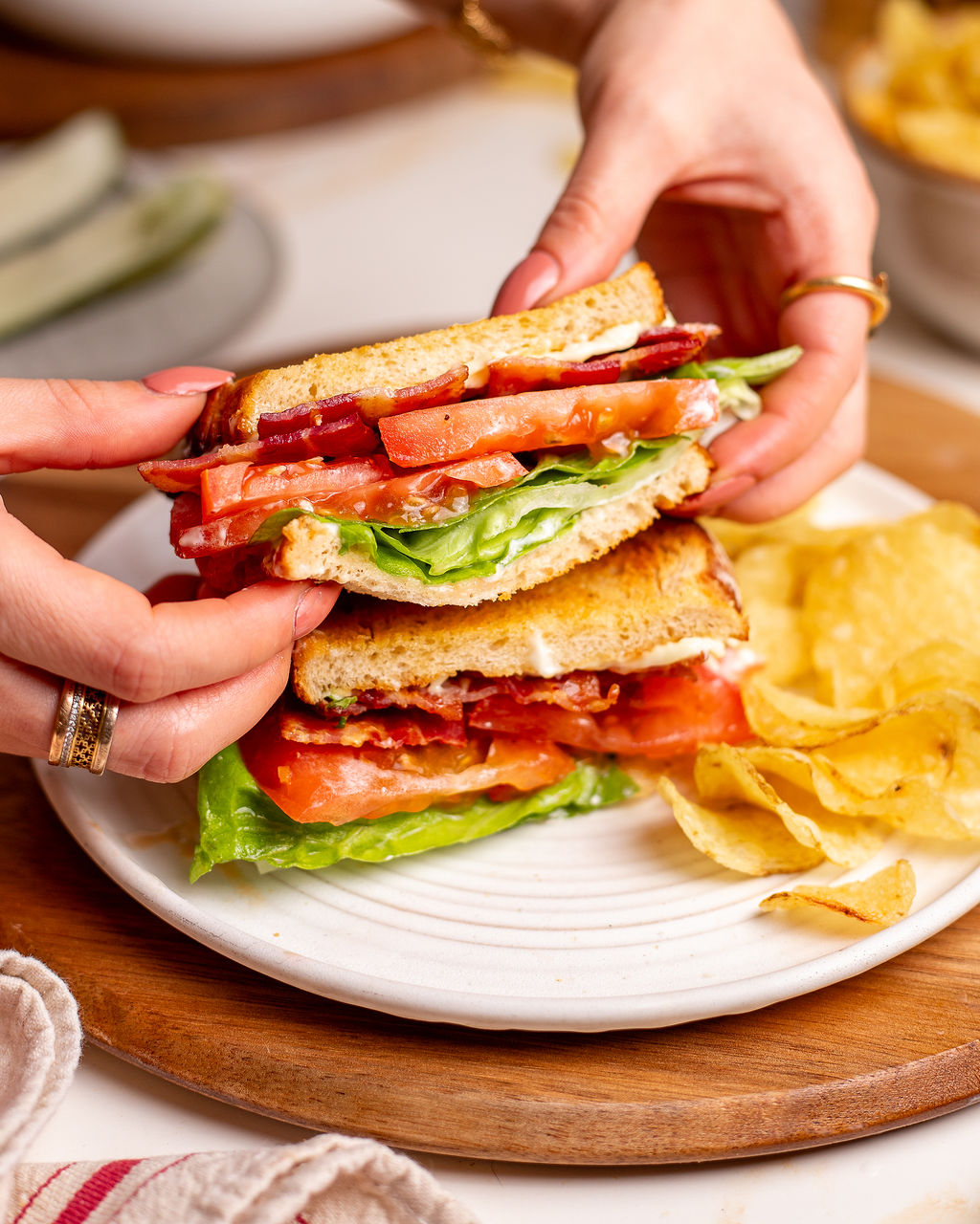 Two hands grabbing a delicious BLT sandwich.