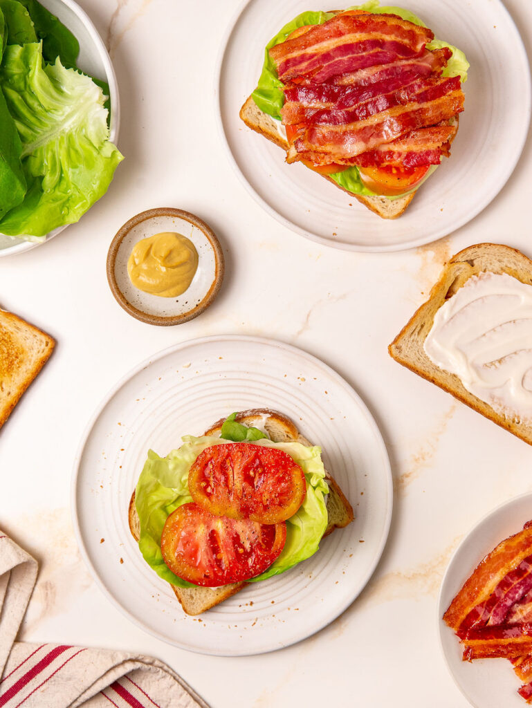 Two open-faced BLT sandwiches on white plates.