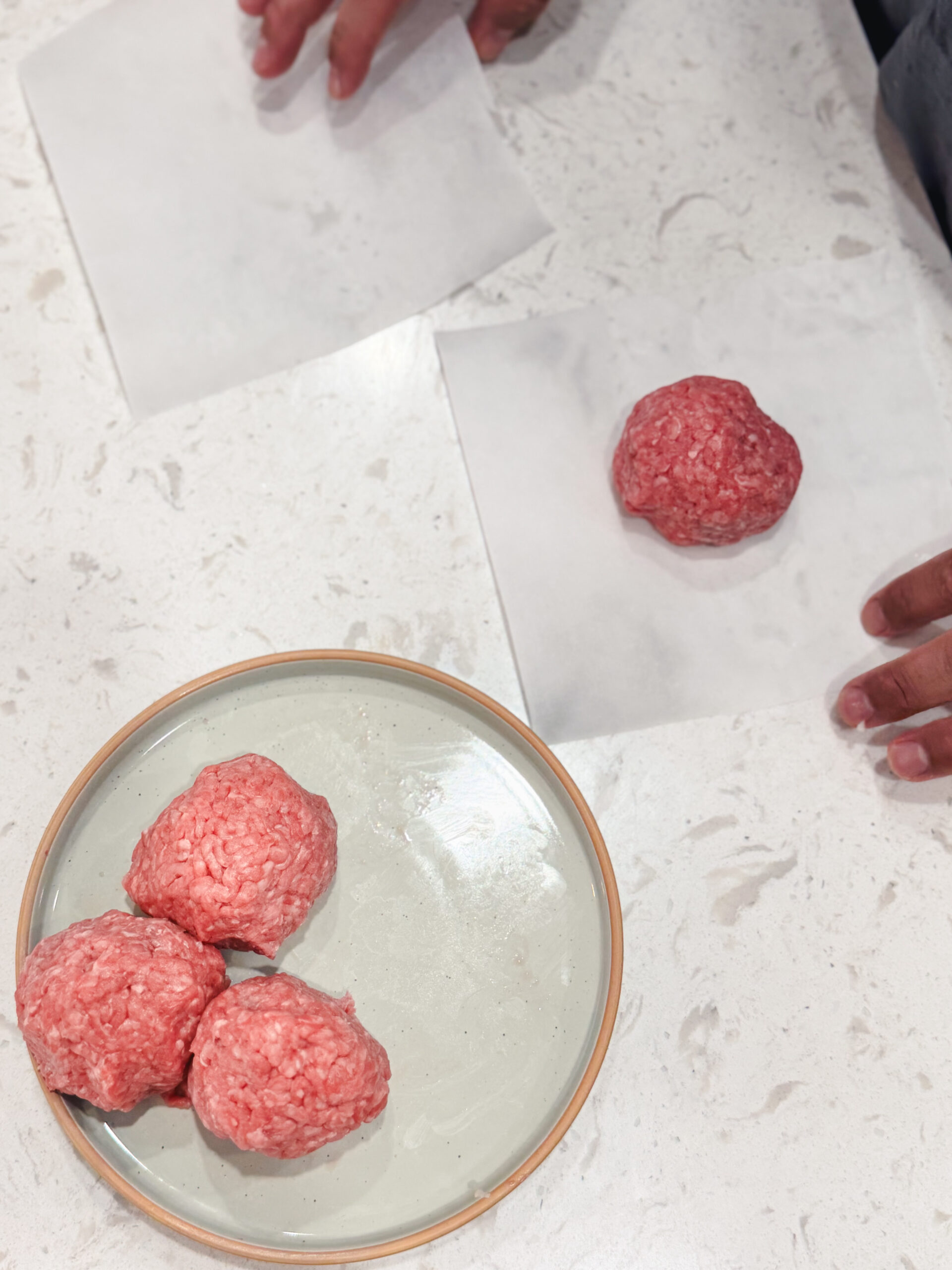 Adding balls of ground beef to parchment paper for smashing.