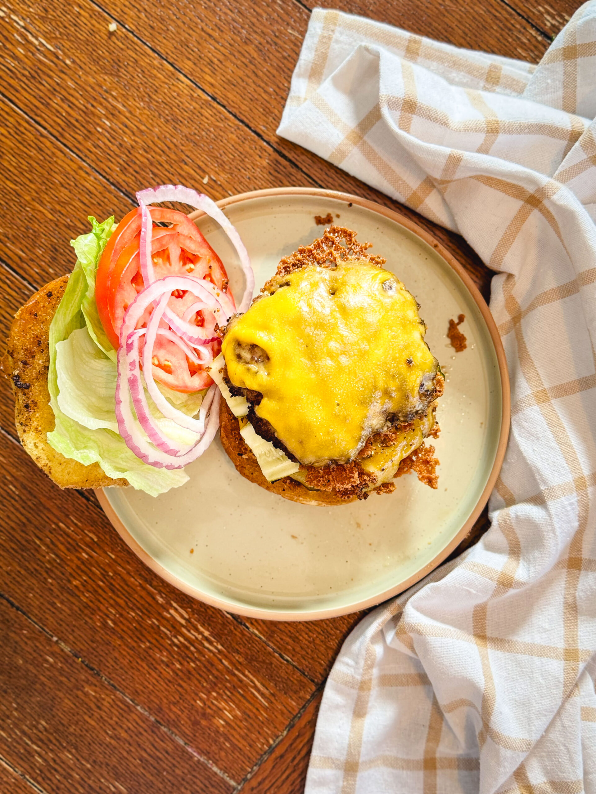 An open-faced smash burger with melted cheese, lettuce, tomato, and onion.