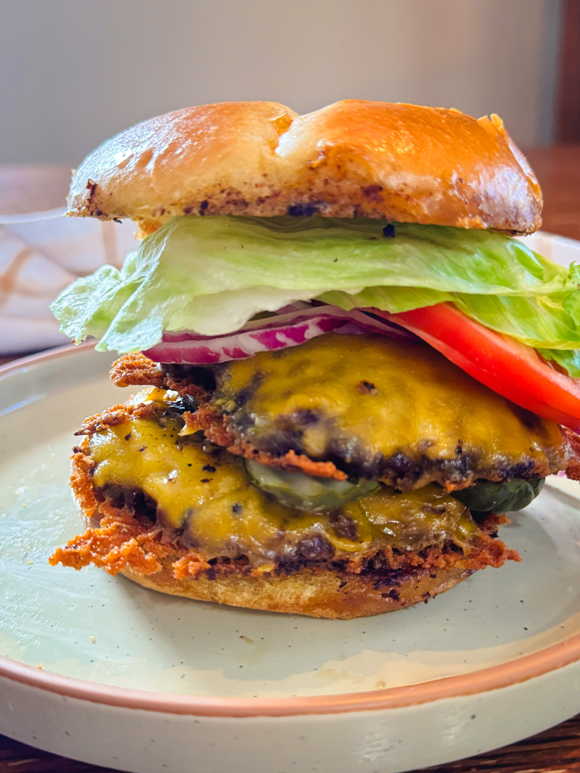 A stacked smash burger on a white plate with lettuce, tomato, and cheese.
