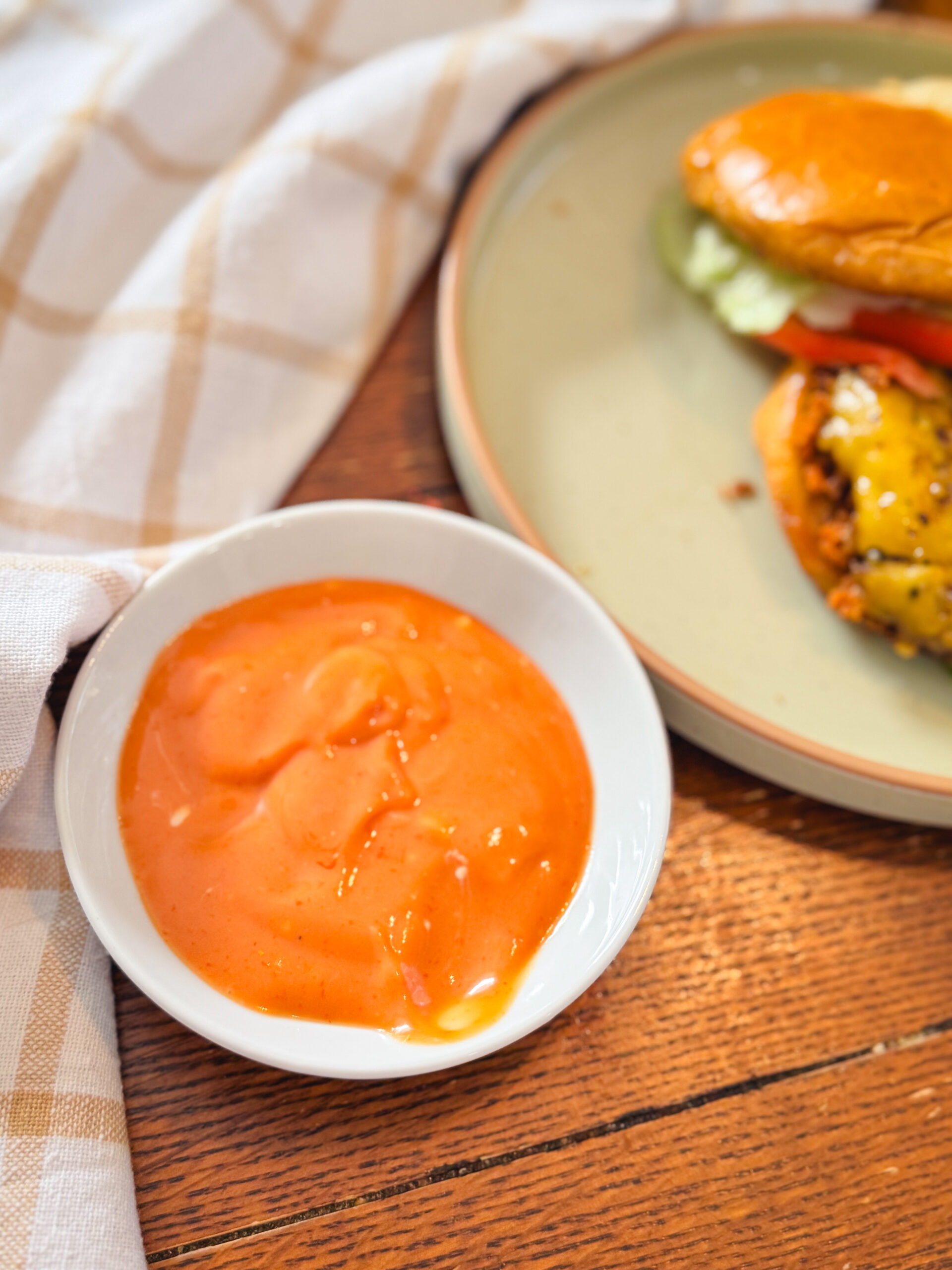 A white dish of my best damn burger sauce next to a juicy burger.