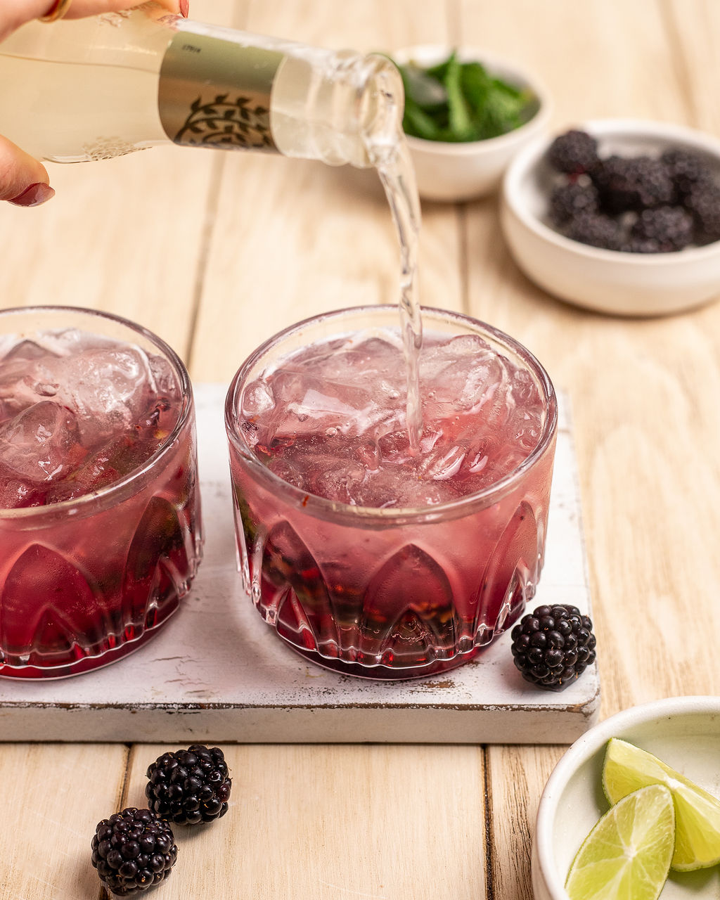 Pouring blackberry mule mocktail into two glasses on a serving platter.