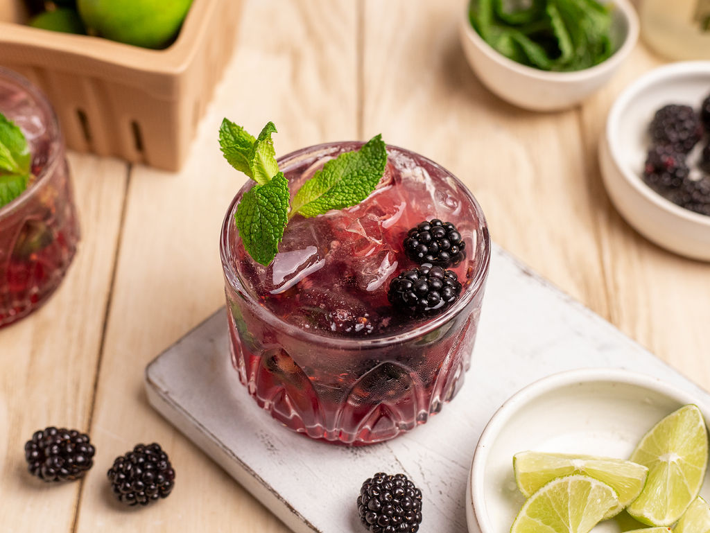 Blackberry mule garnished with fresh blackberries and mint surrounded by ingredients.