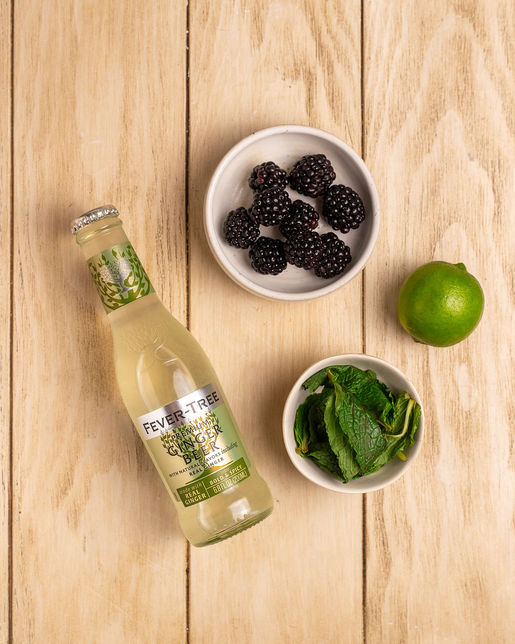 Ingredients for blackberry mule on a light wooden surface.