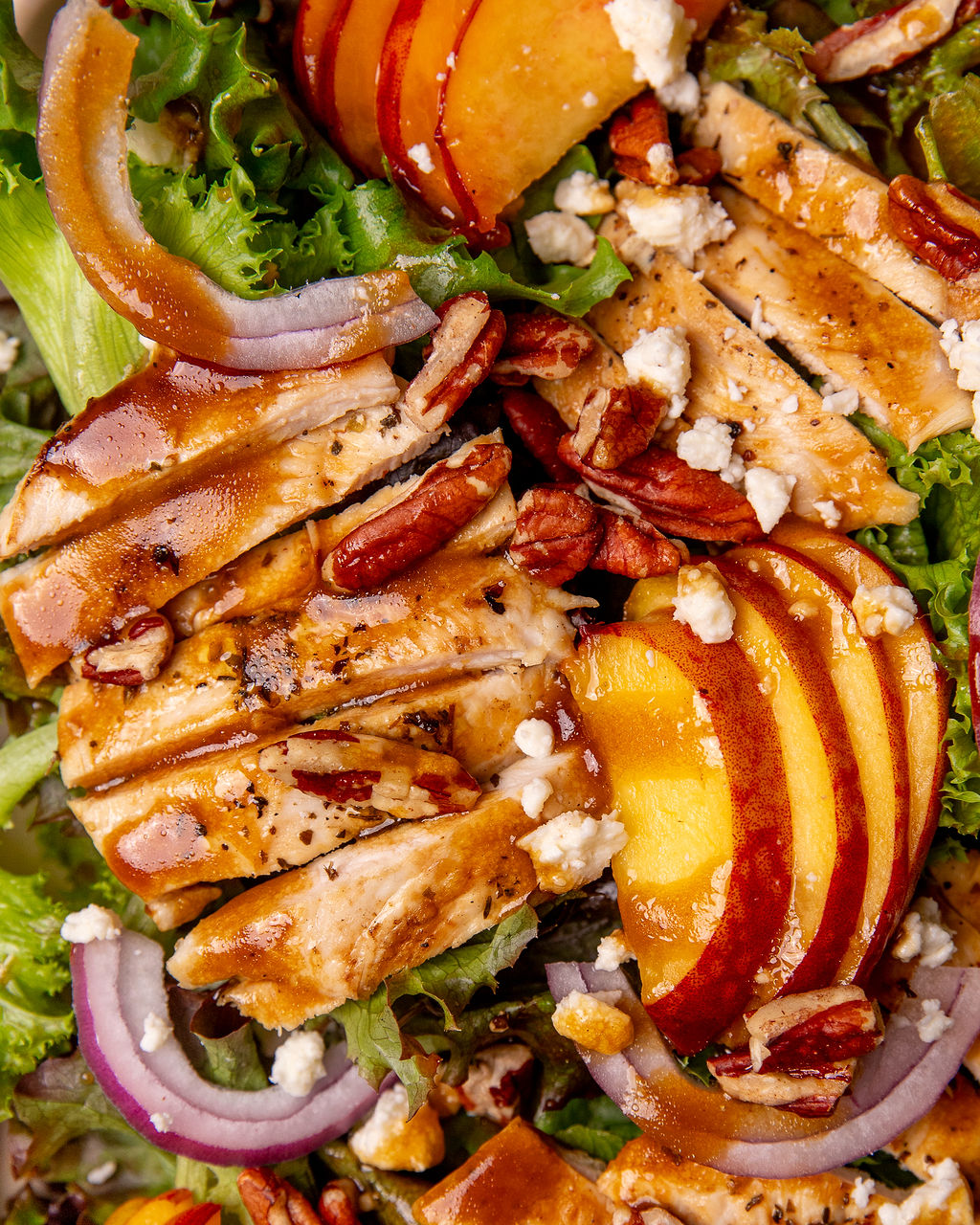 Close up of grilled chicken and peach salad with onion, goat cheese, and dressing.
