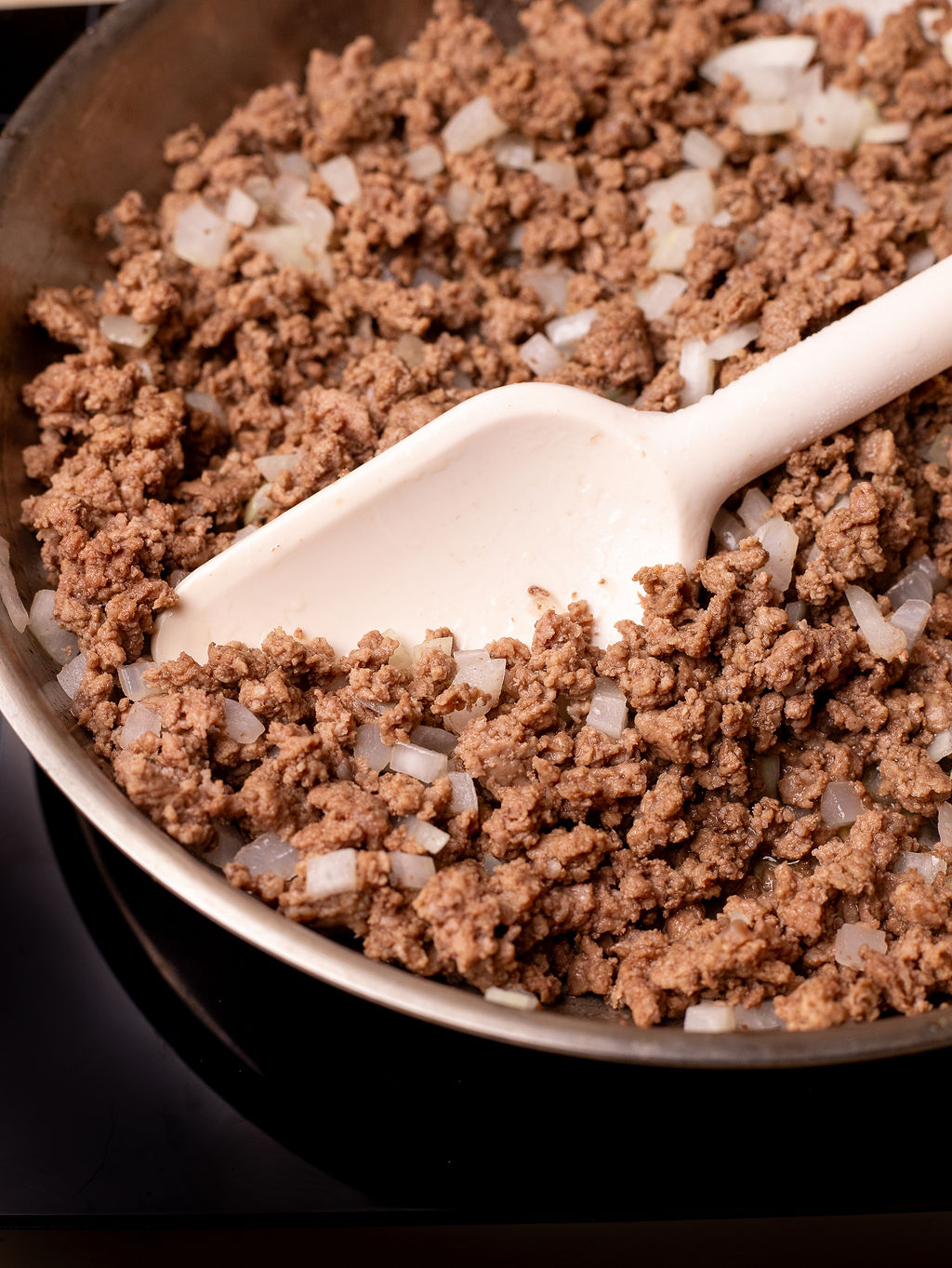 Browned beef and onions in a skillet with a spatula.