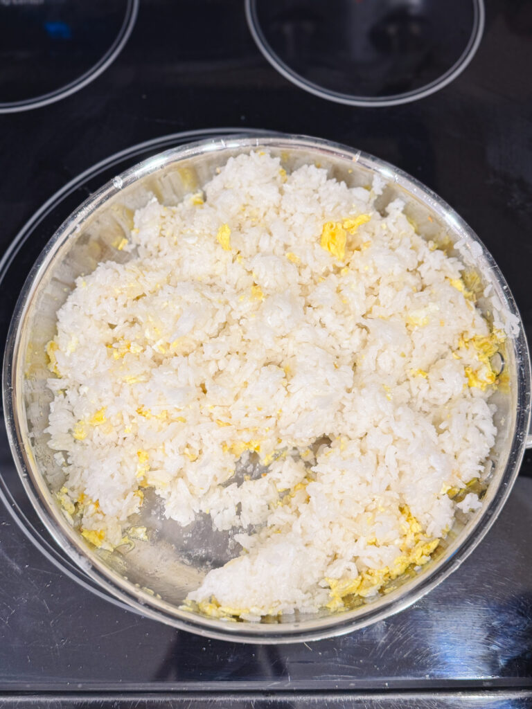 Cooked rice in a skillet with eggs for making fried rice.