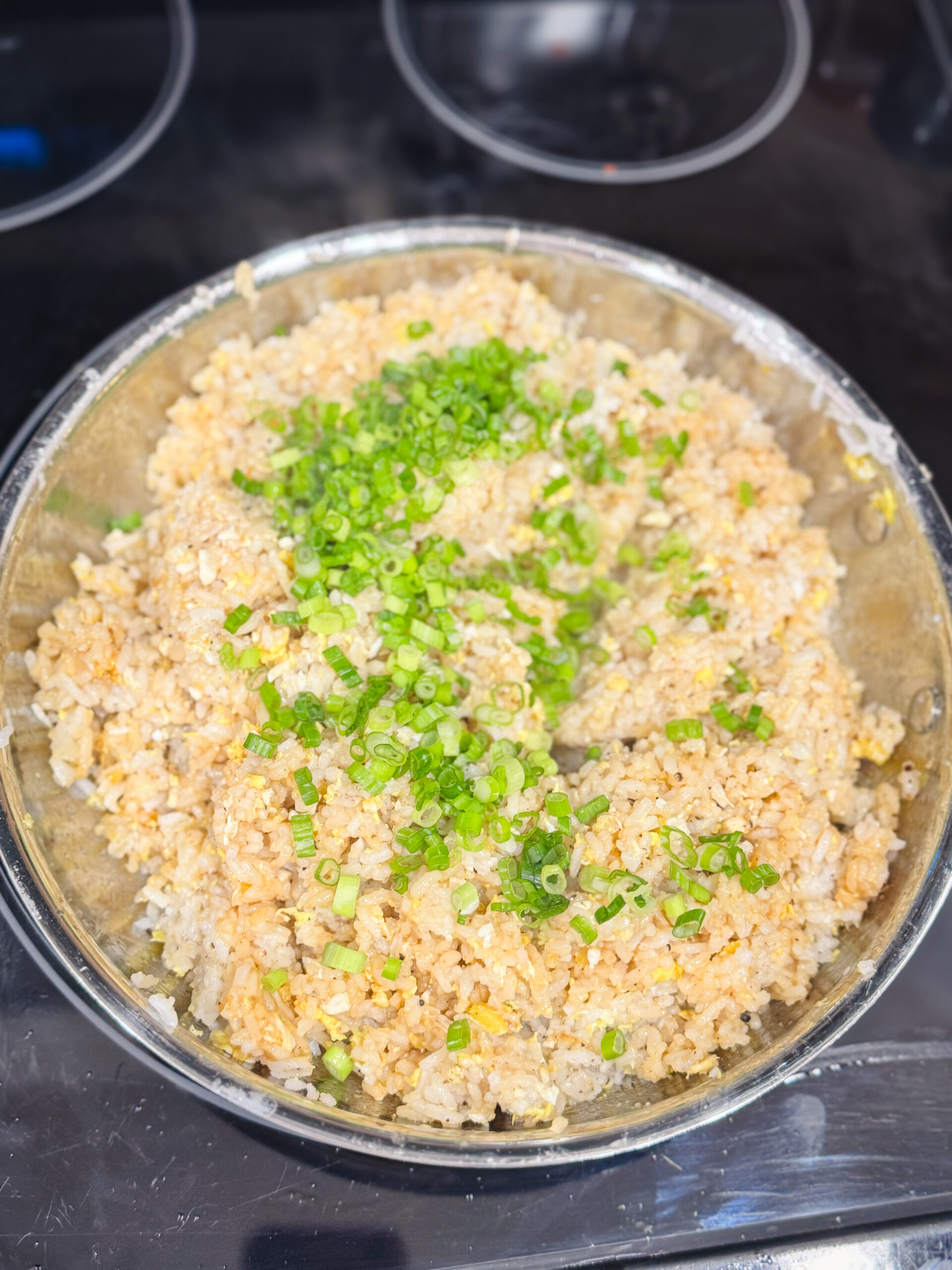 Adding scallions to fried rice in a skillet.