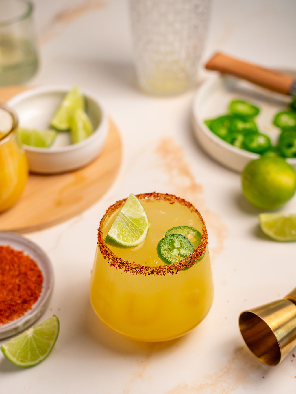 Spicy mockarita in a glass with Tajin on the rim and lime and jalapeno as garnish. Ingredients in the background.