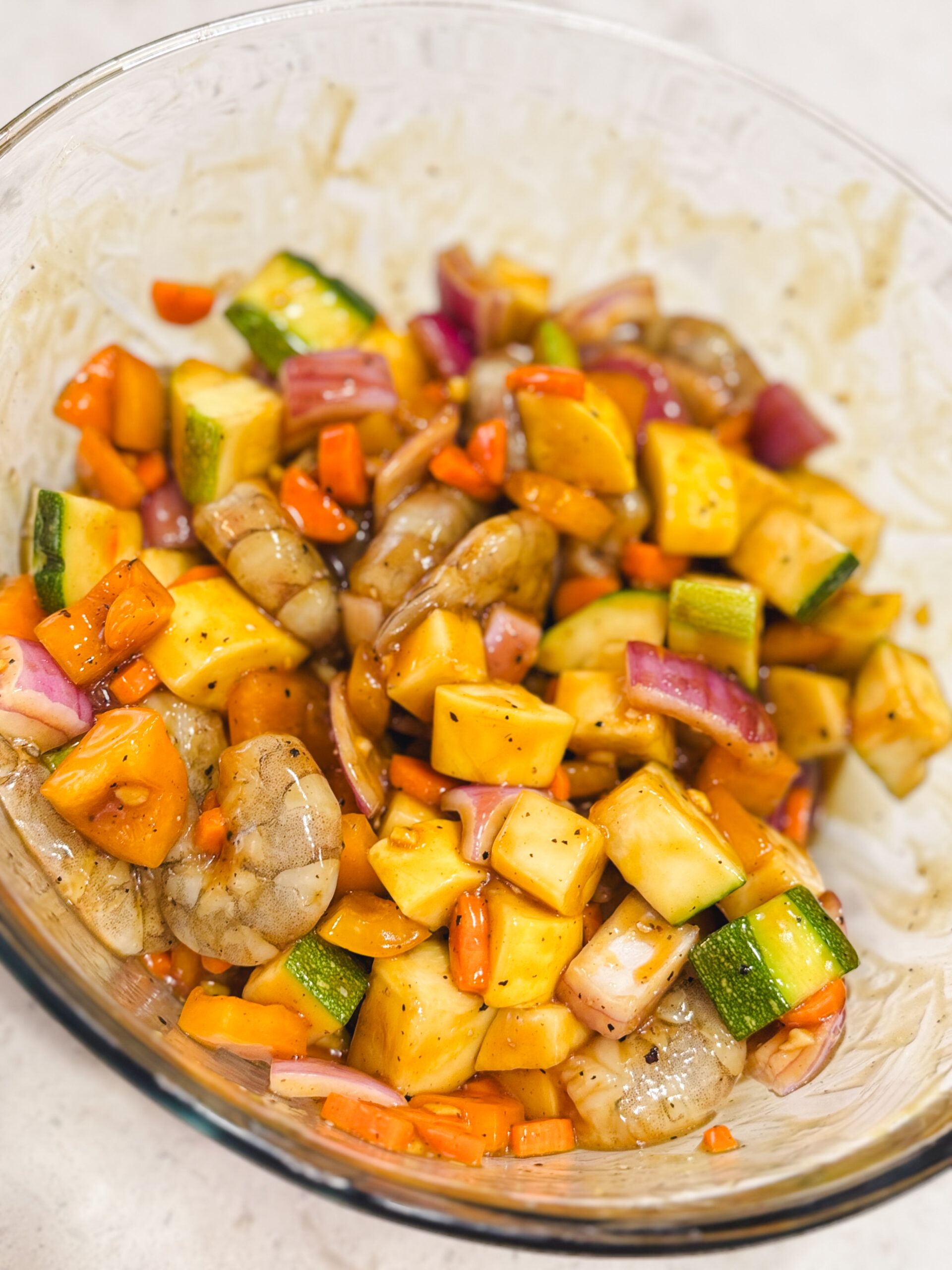Fresh shrimp and summer veggies in a white bowl coated in teriyaki sauce.