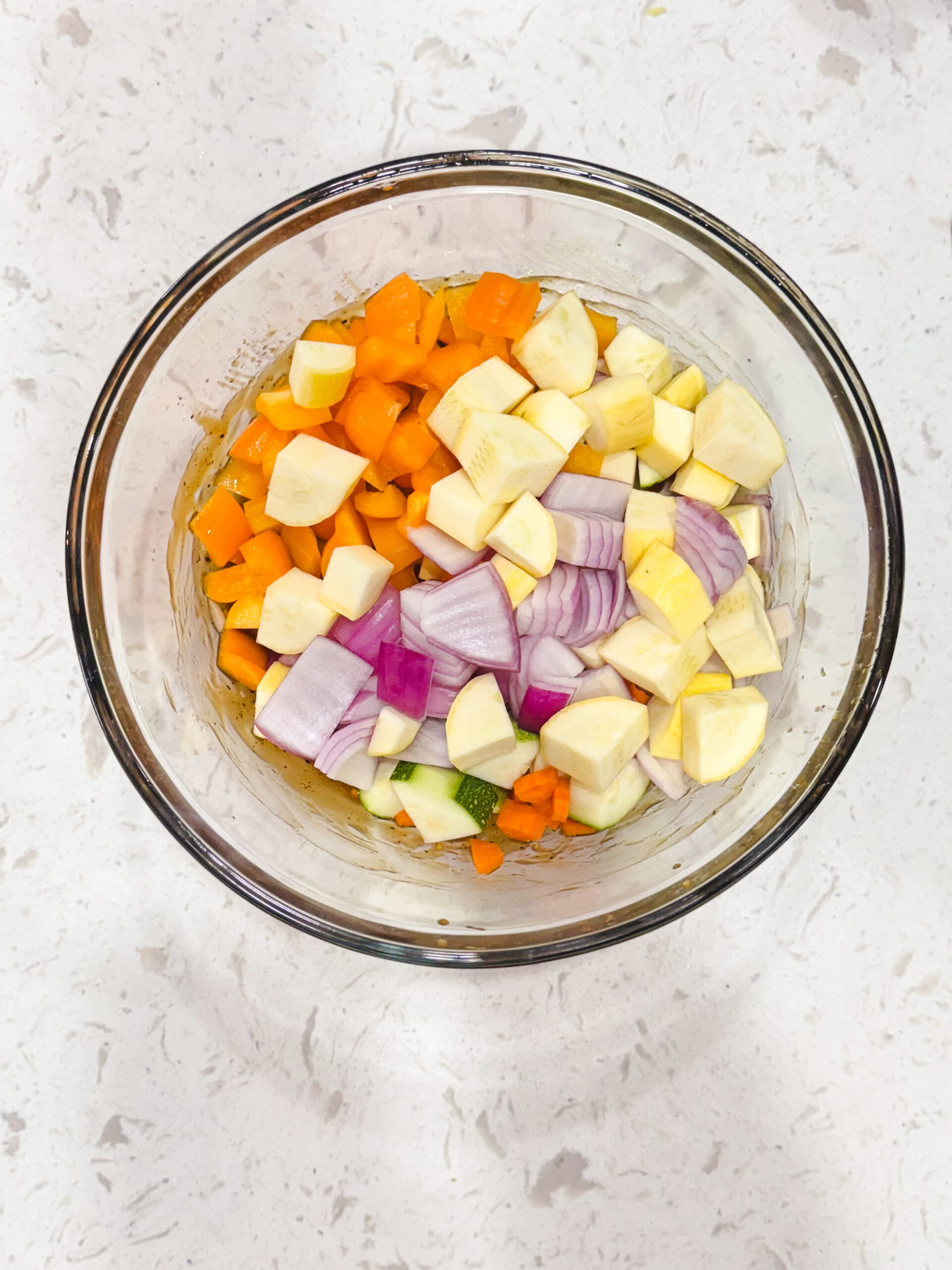 Zucchini, yellow squash, red onion, and bell pepper in a glass bowl.