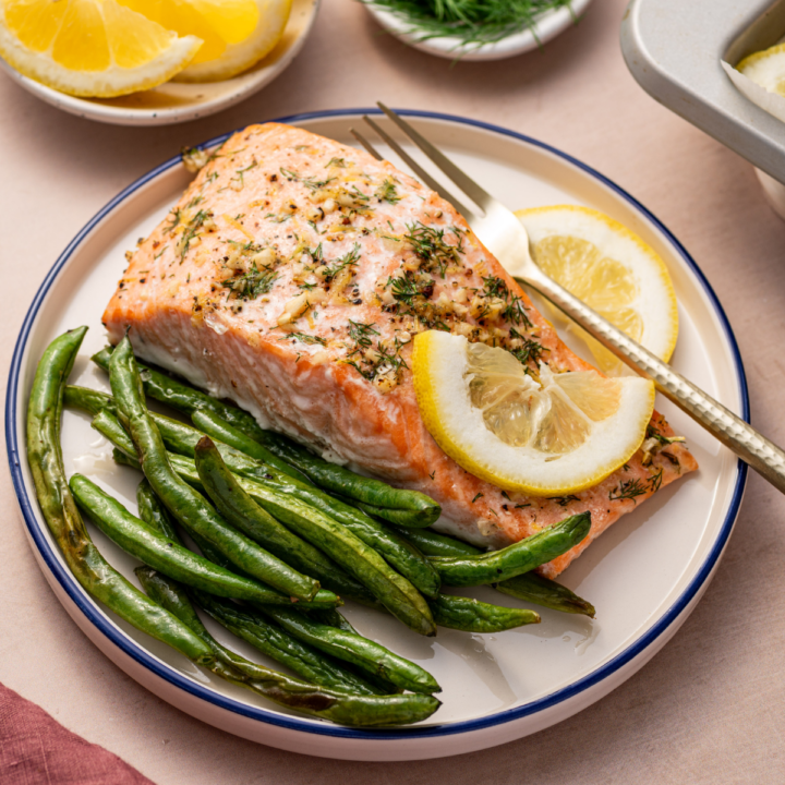 A serving of lemon dill salmon on a white plate with a side of green beans,
