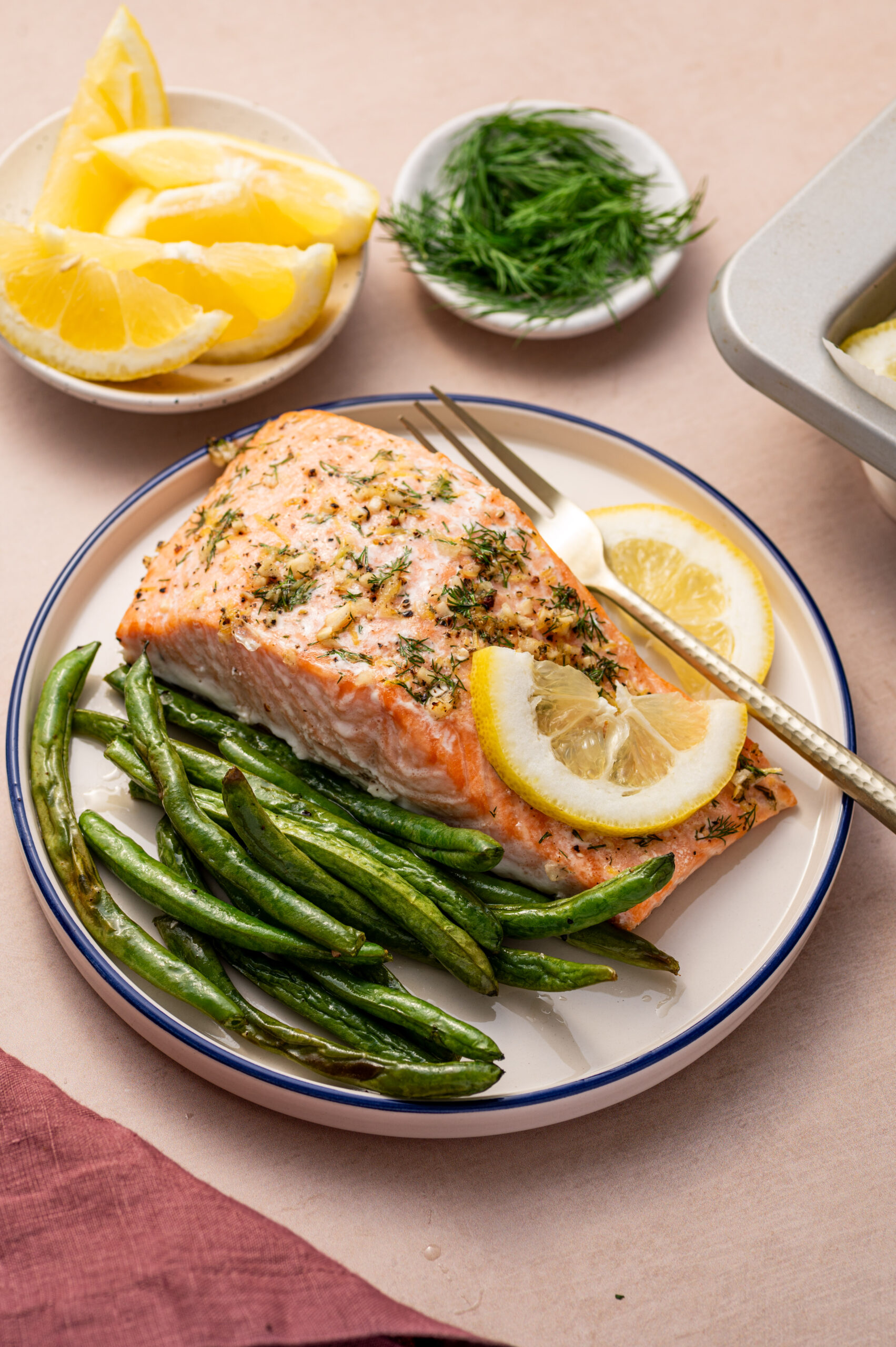 A serving of lemon dill salmon on a white plate with a side of green beans,