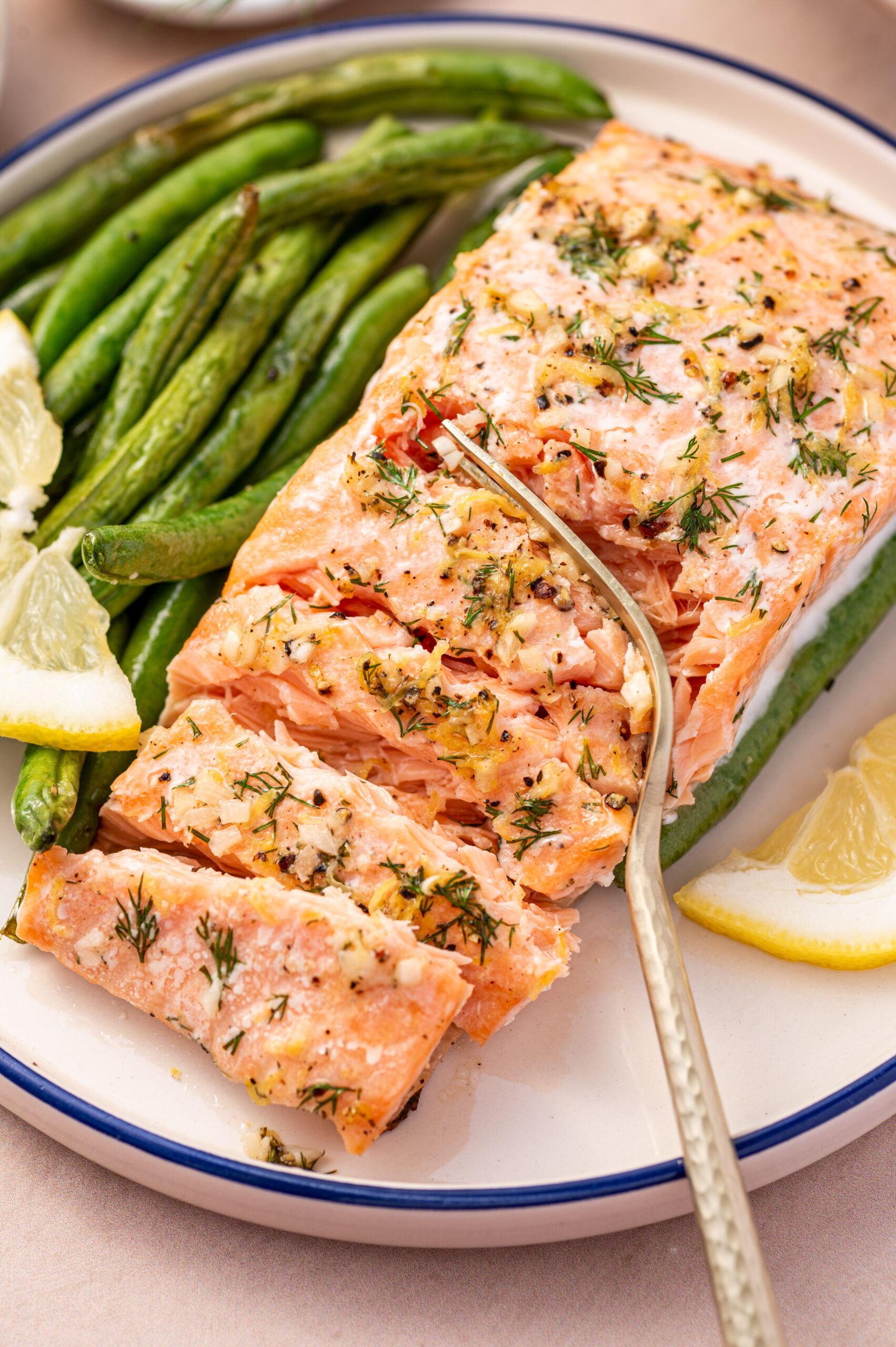 Cutting into a lemon dill salmon fillet with green beans on the side.