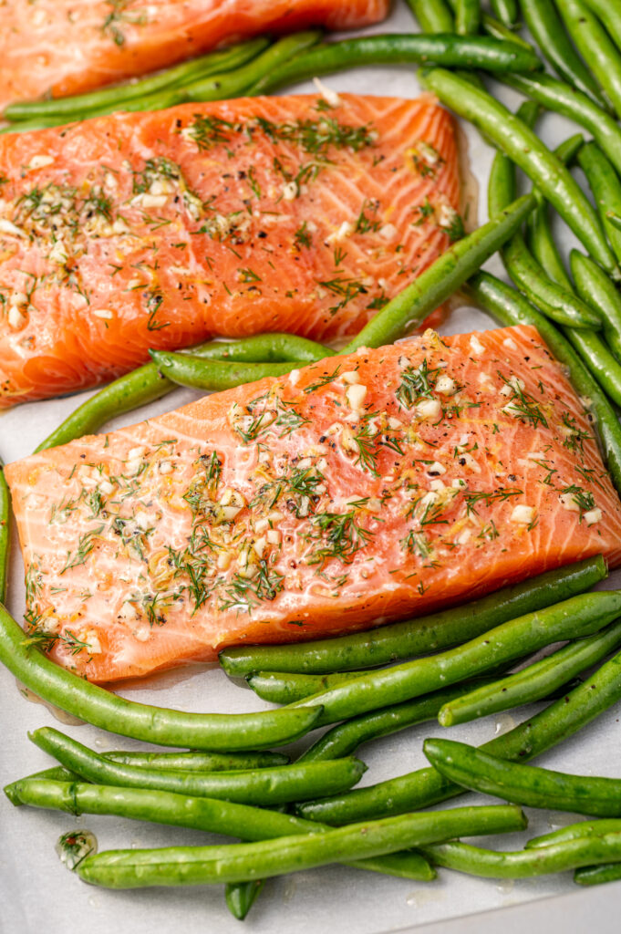 Close-up of lemon dill salmon fillets on a sheet pan with green beans, ready to go in the oven.