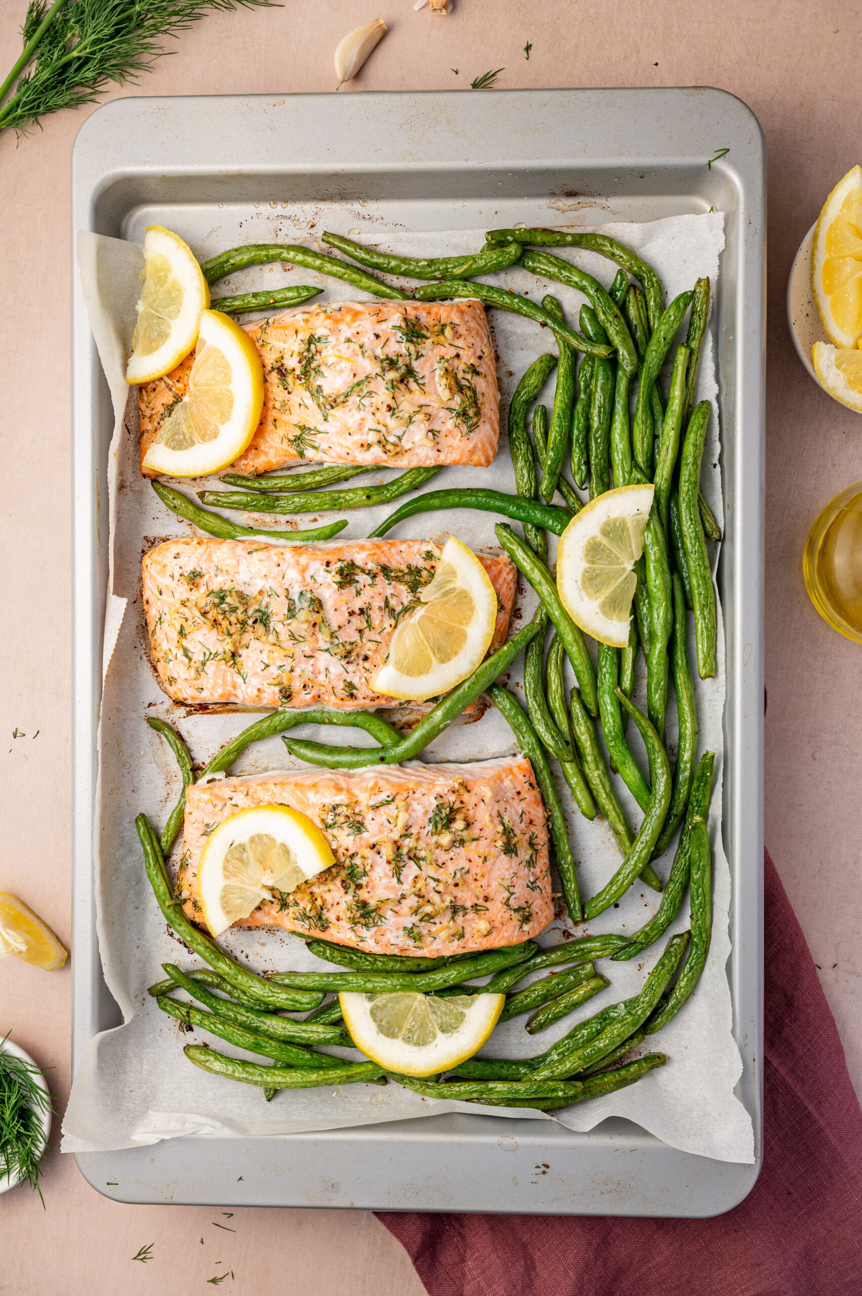 Three lemon dill salmon fillets on a sheet pan with green beans and lemon slices.