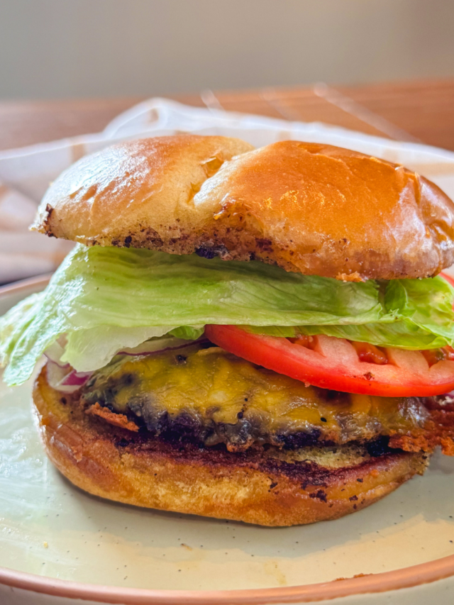 A stacked smash burger with lettuce, tomato, and cheese.