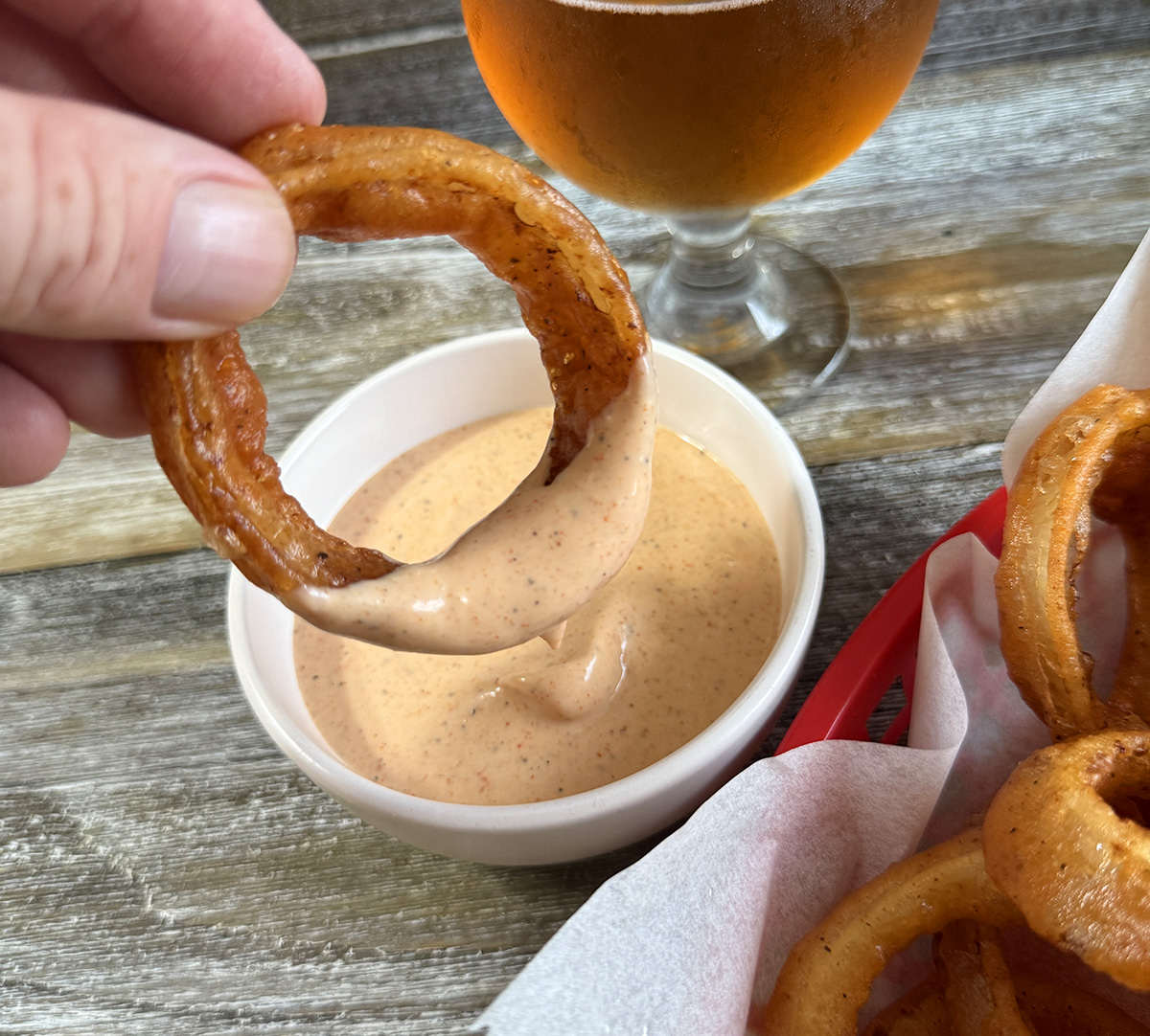 Dipping homemade beer battered onion rings into dipping sauce.