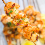 A skewer of grilled shrimp with grill marks and parsley as a garnish.