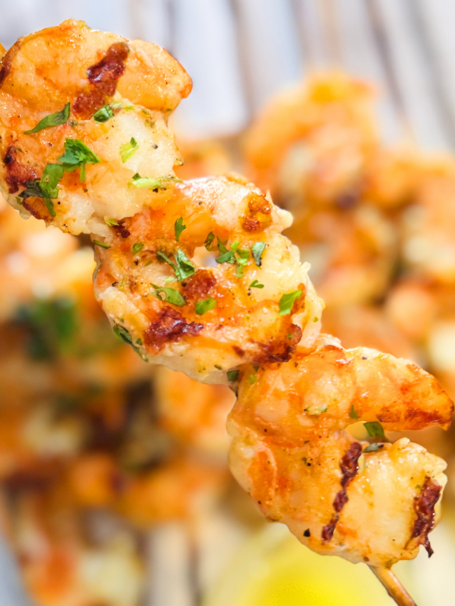 A skewer of grilled shrimp with grill marks and parsley as a garnish.