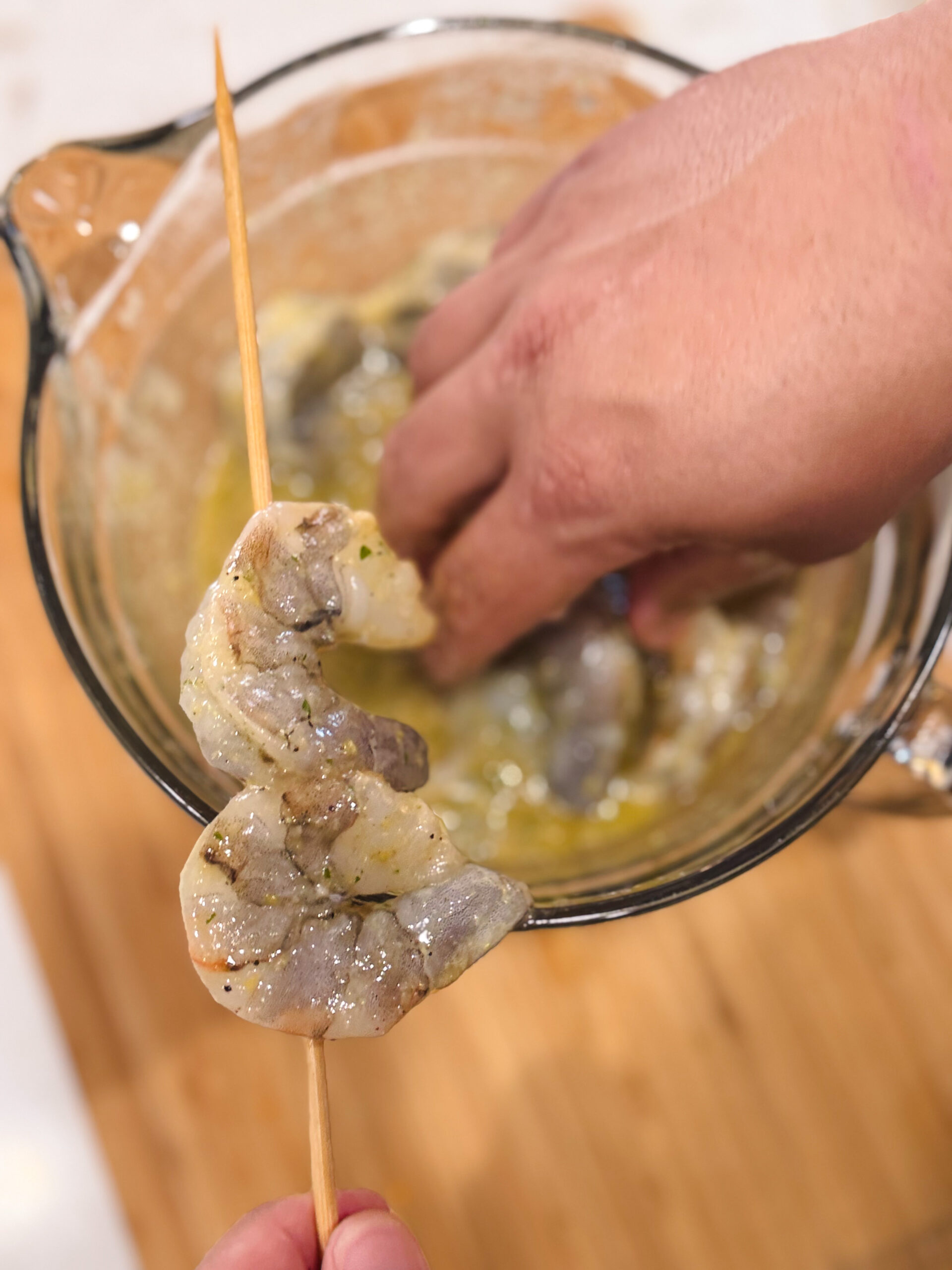 Adding raw shrimp to wooden skewers.