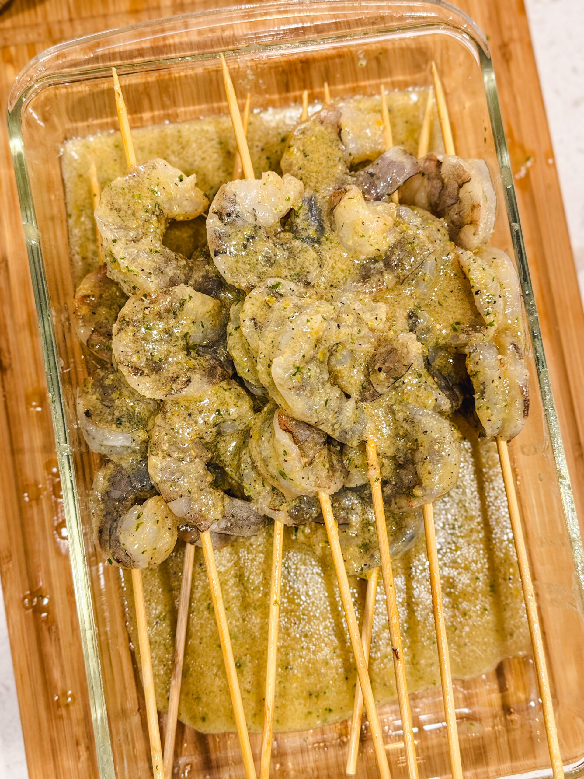 Skewered shrimp soaked in marinade inside a glass container.