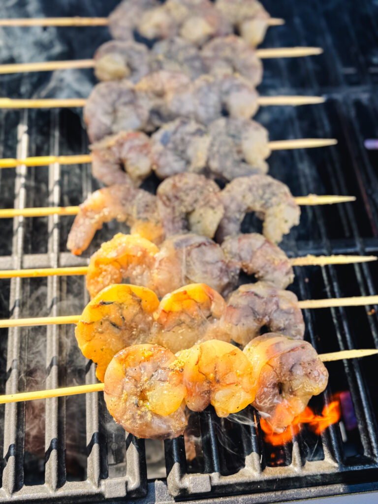 Close-up of skewered shrimp on the grill beginning to cook with a flicker of flame.