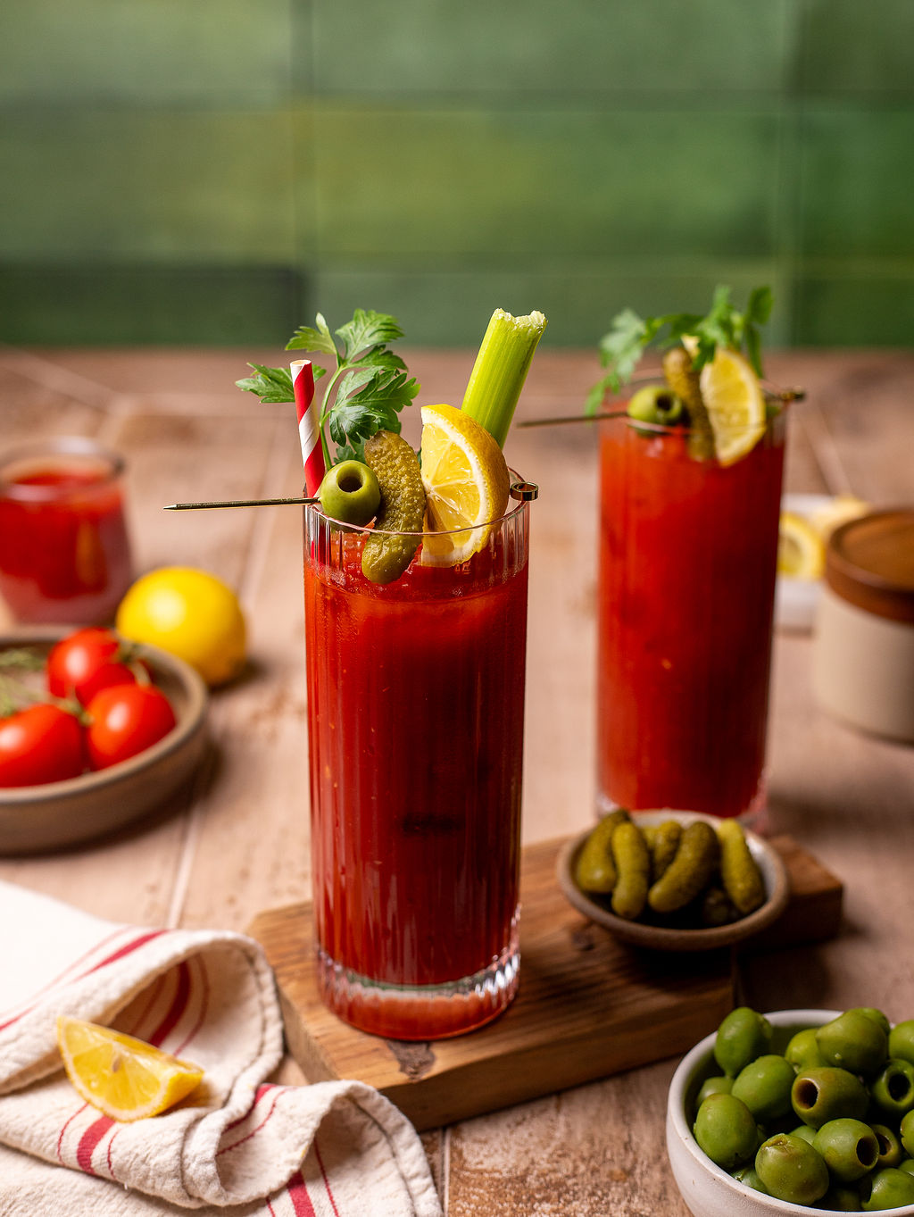 Two bloody Mary mocktails with pickles, sliced lemon, celery, and parsley as a garnish.