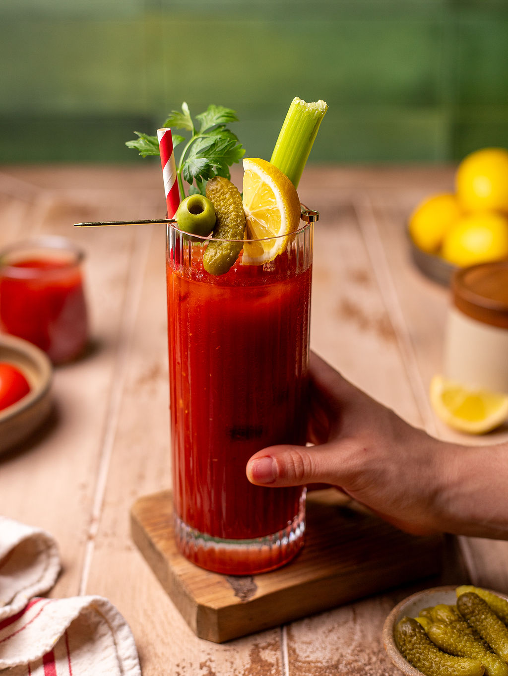 A hand grabbing a bloody Mary mocktail with pickles, sliced lemon, celery, and parsley as a garnish.