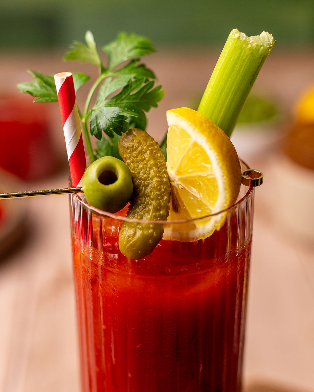 Close-up of a bloody Mary mocktail dressed with pickles, sliced lemon, celery, and parsley.