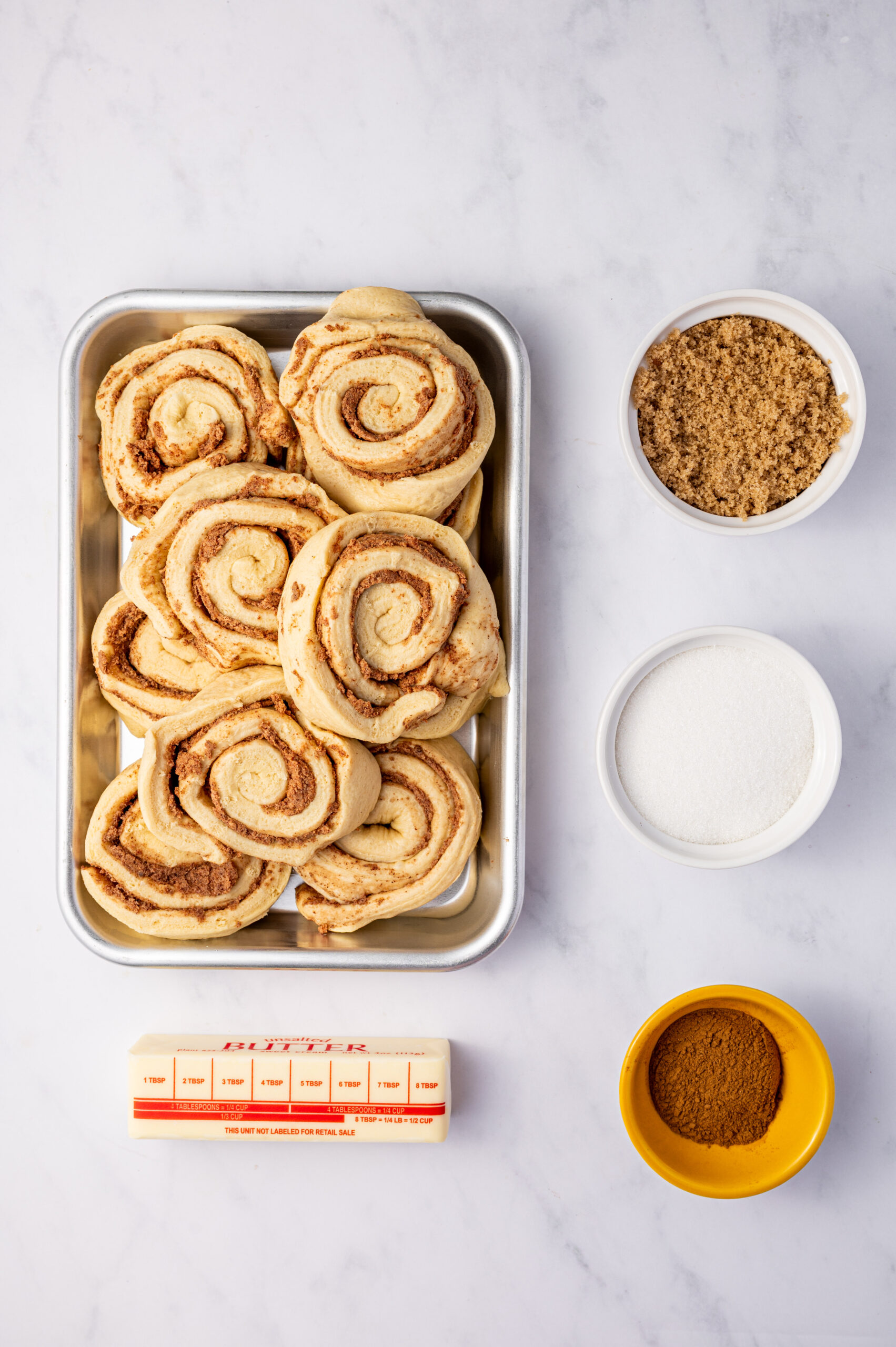 Ingredients for cinnamon roll monkey bread on a gray marble surface.