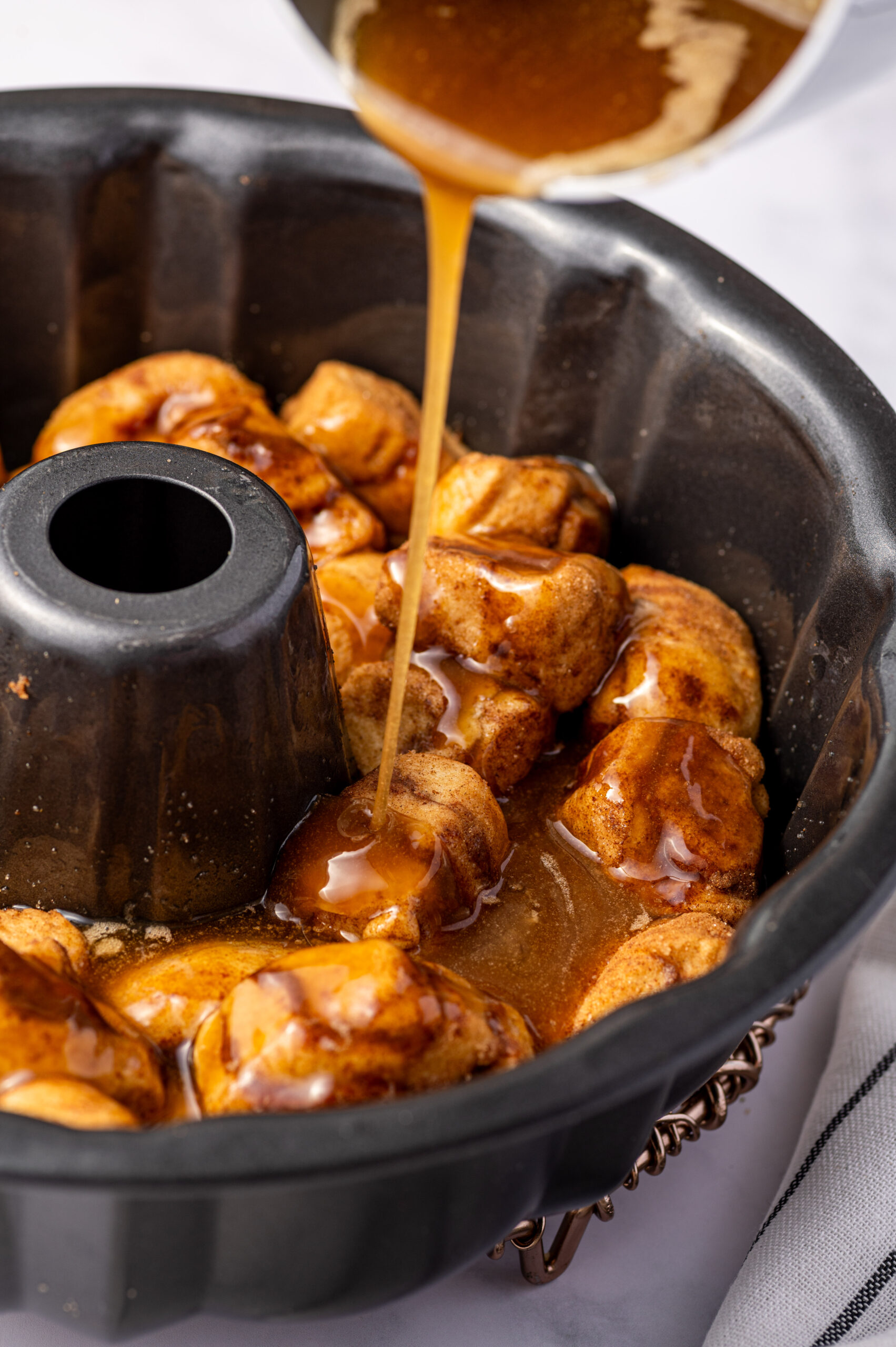 Adding melted butter and brown sugar to a bundt cake pan full of cut up cinnamon rolls.