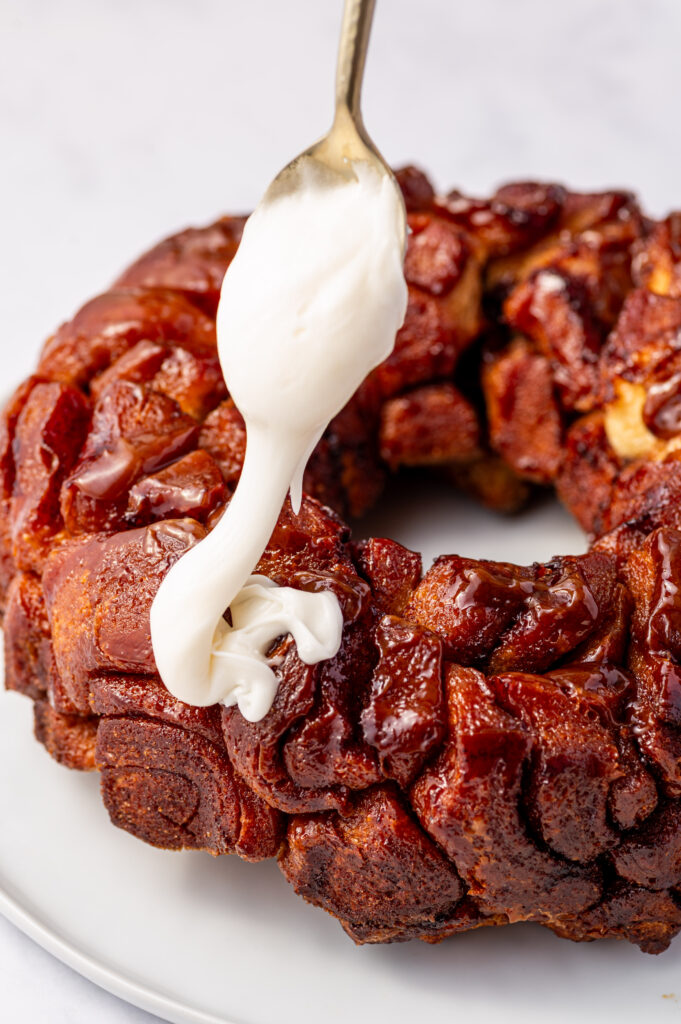 Adding icing to cinnamon roll monkey bread with a spoon.