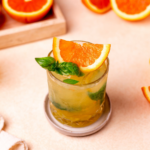 A glass of citrus basil smash with sliced orange and basil as a garnish.