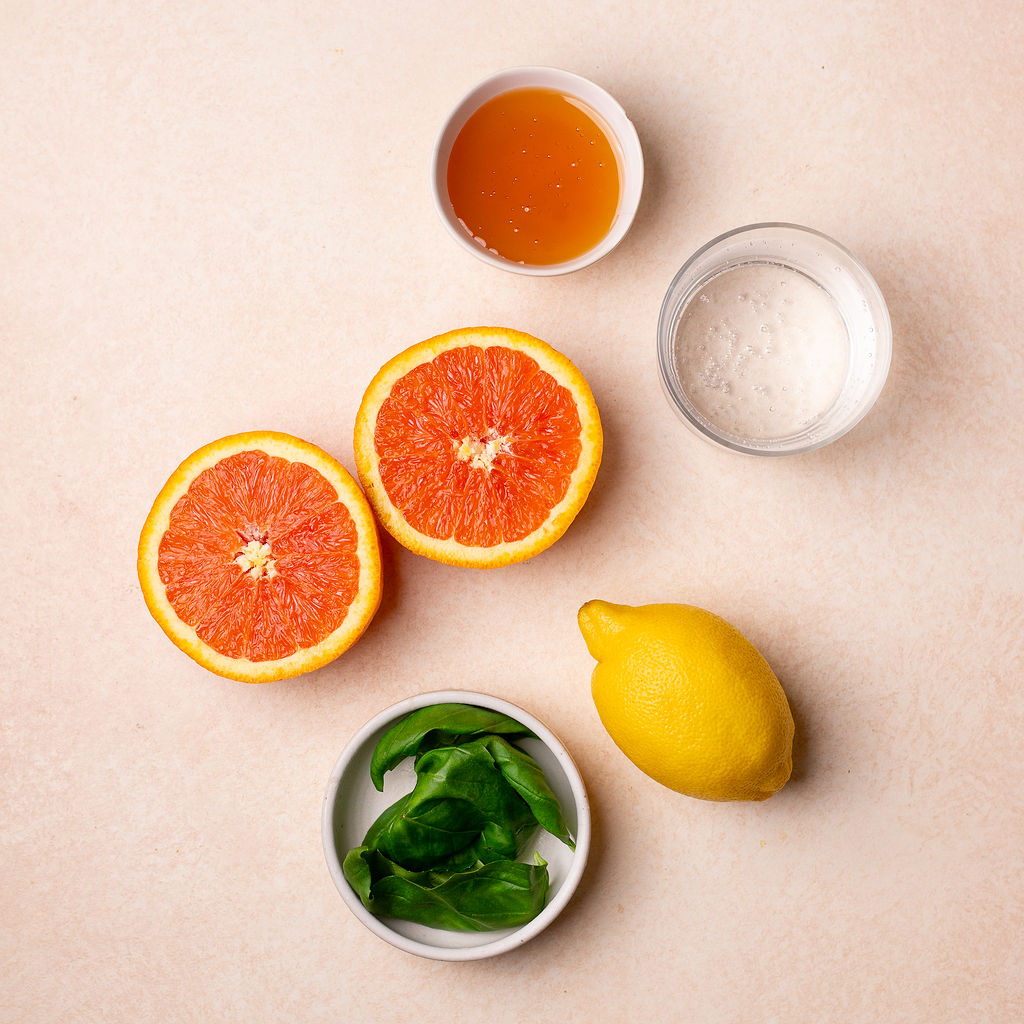 Ingredients for citrus basil smash on a slightly pink surface.