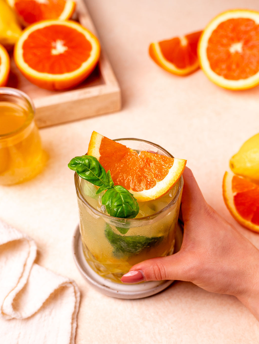 A hand grabbing a glass of citrus basil smash garnished with basil and sliced orange.