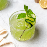 Cucumber cooler in a glass garnished with a cucumber ribbon and a sprig of mint.
